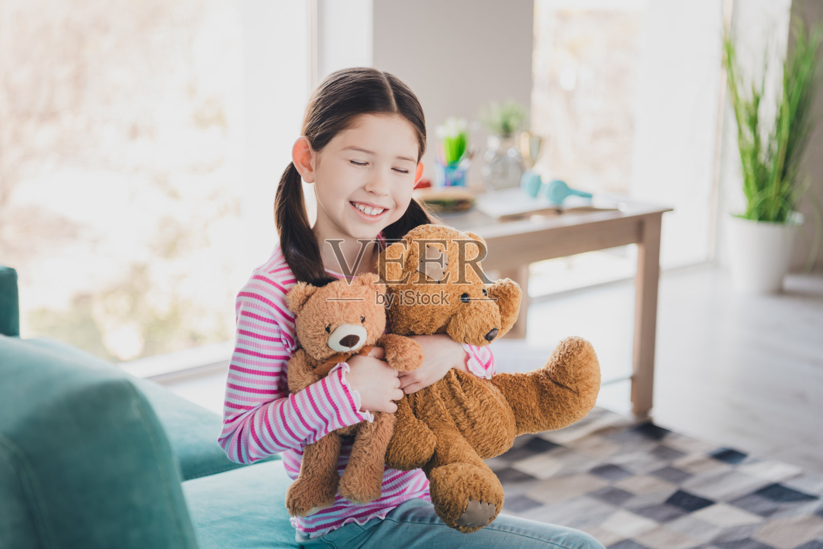 年轻有趣的孩子的照片，小黑发女孩呆在家里度过周末，她最喜欢的玩具毛绒泰迪熊被隔离在她的房间里照片摄影图片