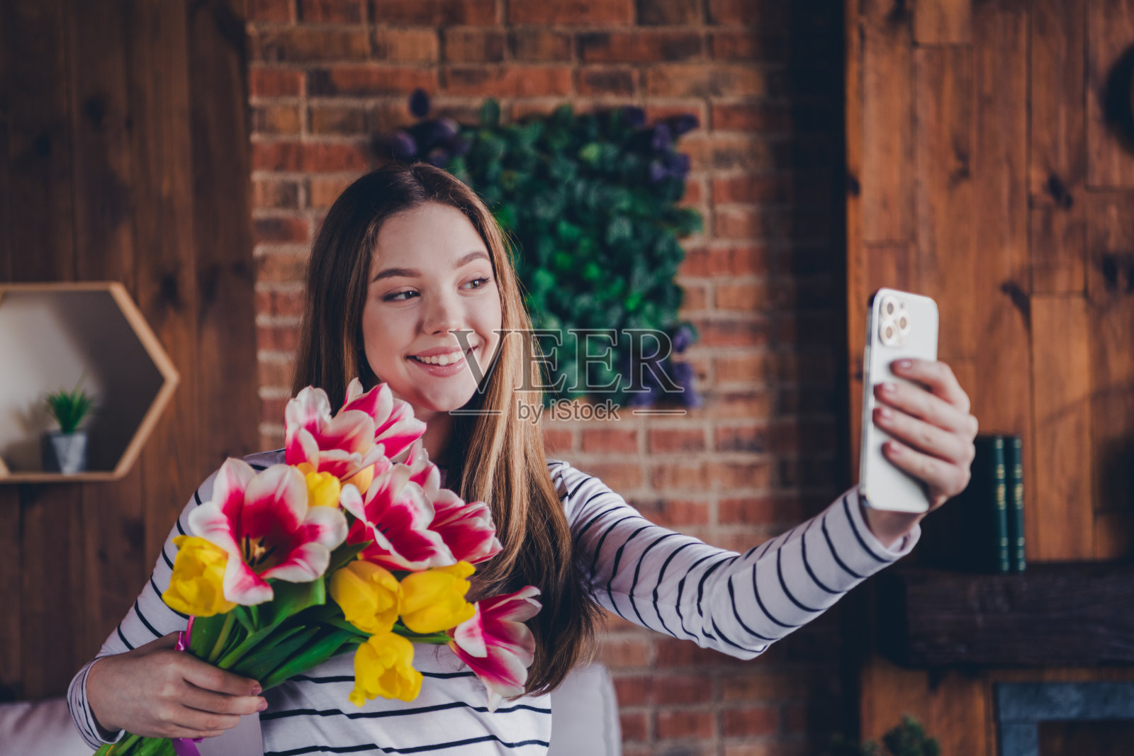 照片迷人的少女手持鲜花花束郁金香自拍照片穿着条纹装昼光家室内客厅照片摄影图片