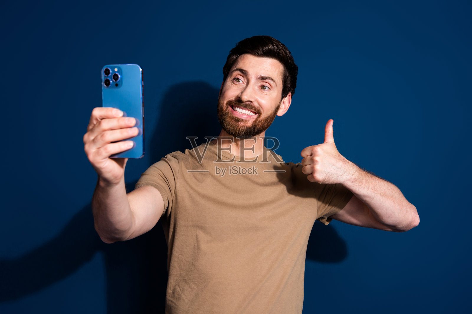 照片年轻英俊的家伙黑发使用智能手机拍摄显示像符号孤立在深蓝色的背景照片摄影图片
