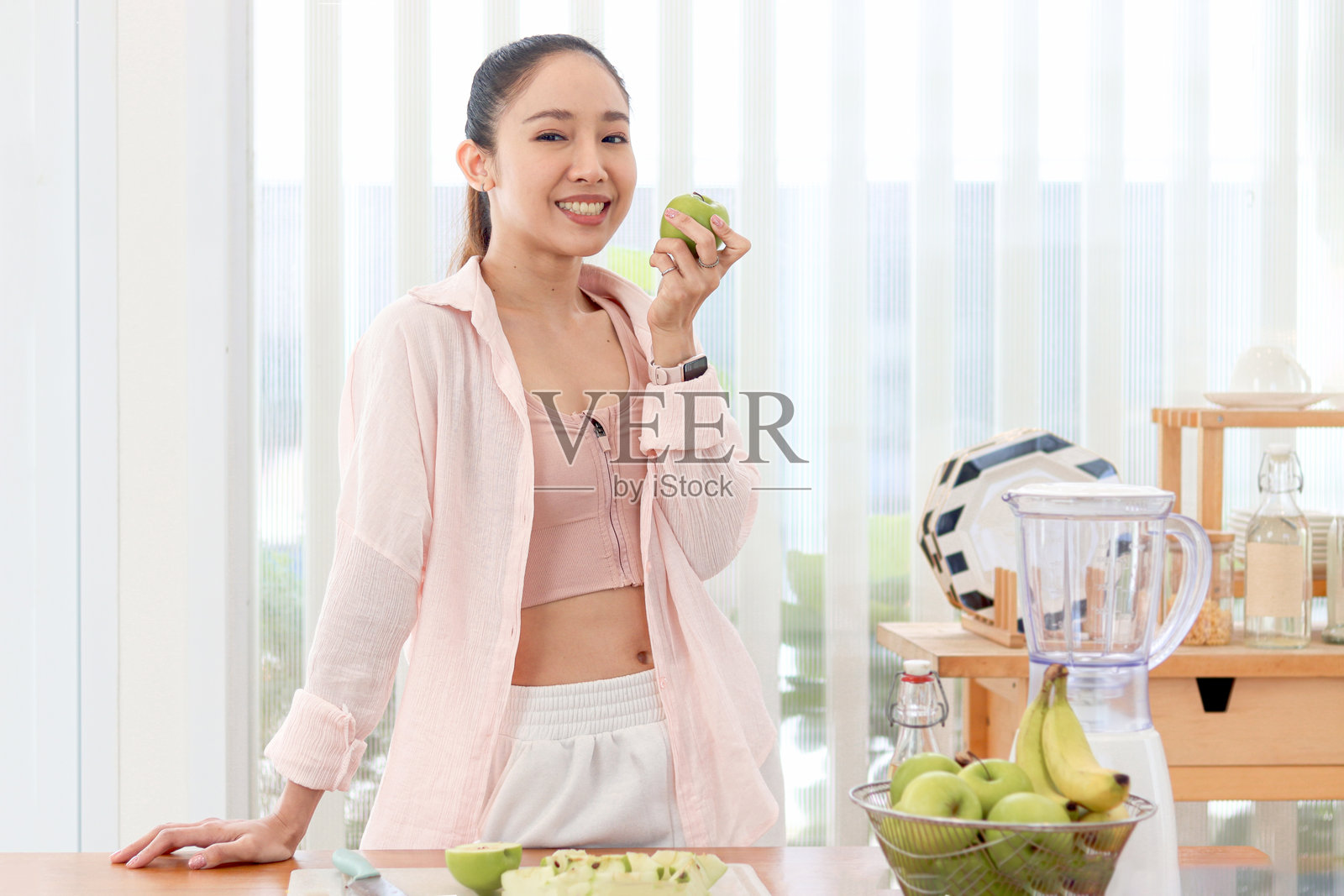 运动女孩在厨房拿着青苹果咬了一口。美丽快乐的亚洲女人拿着果篮。年轻女性为了健康吃水果。减肥、瘦身、健康饮食健身锻炼照片摄影图片