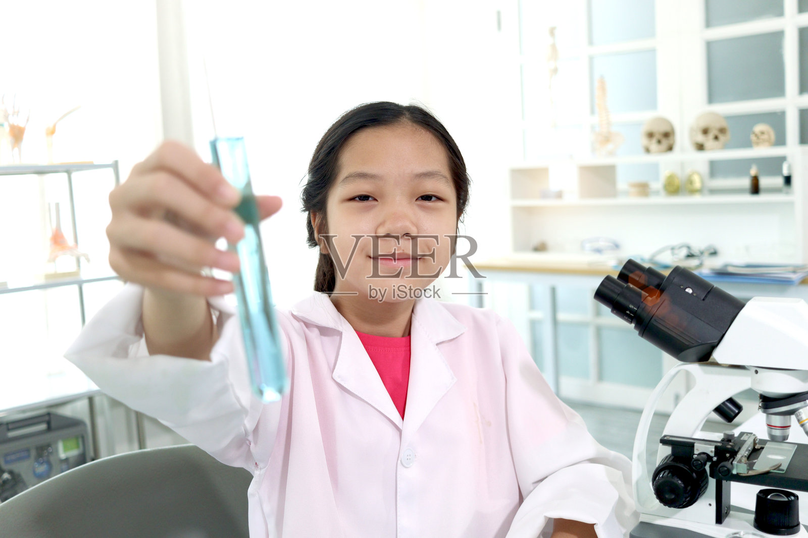 可爱的女学生穿着实验室大褂，展示蓝色的化学药品，向镜头展示试管，做科学实验的孩子，在实验室学习科学实验的年轻科学家学生。亚洲小孩使用显微镜、仪器和实验室设备进行研究。合作伙伴照片摄影图片