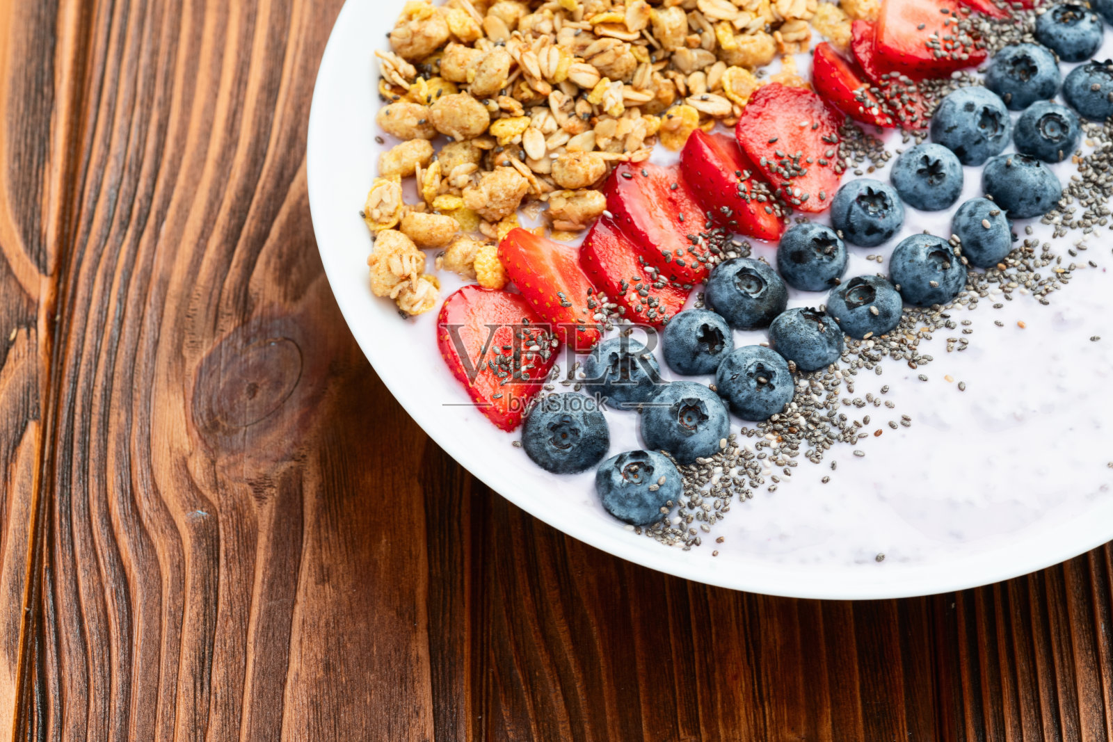 健康早餐。浆果酸奶(草莓、覆盆子、蓝莓、黑莓)、格兰诺拉麦片和奇亚籽。俯视图照片摄影图片