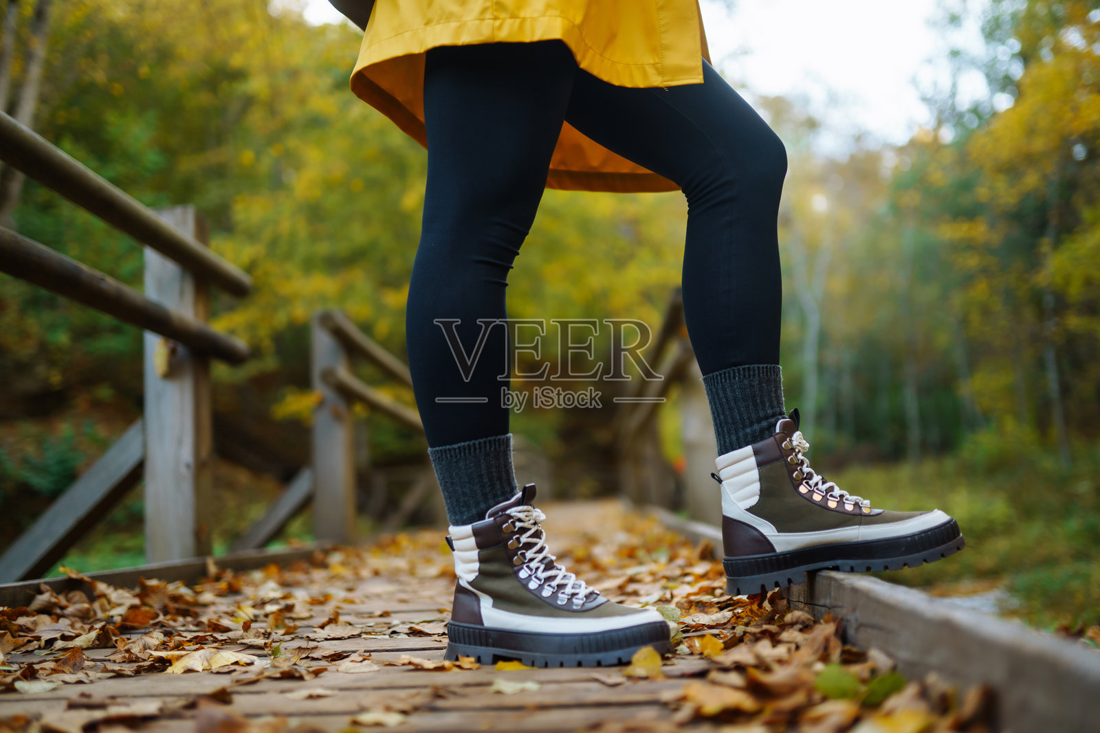 一位徒步旅行者穿着亮黄色的雨衣和结实的靴子，走在生机勃勃的秋天森林里一条树叶覆盖的小路上。照片摄影图片