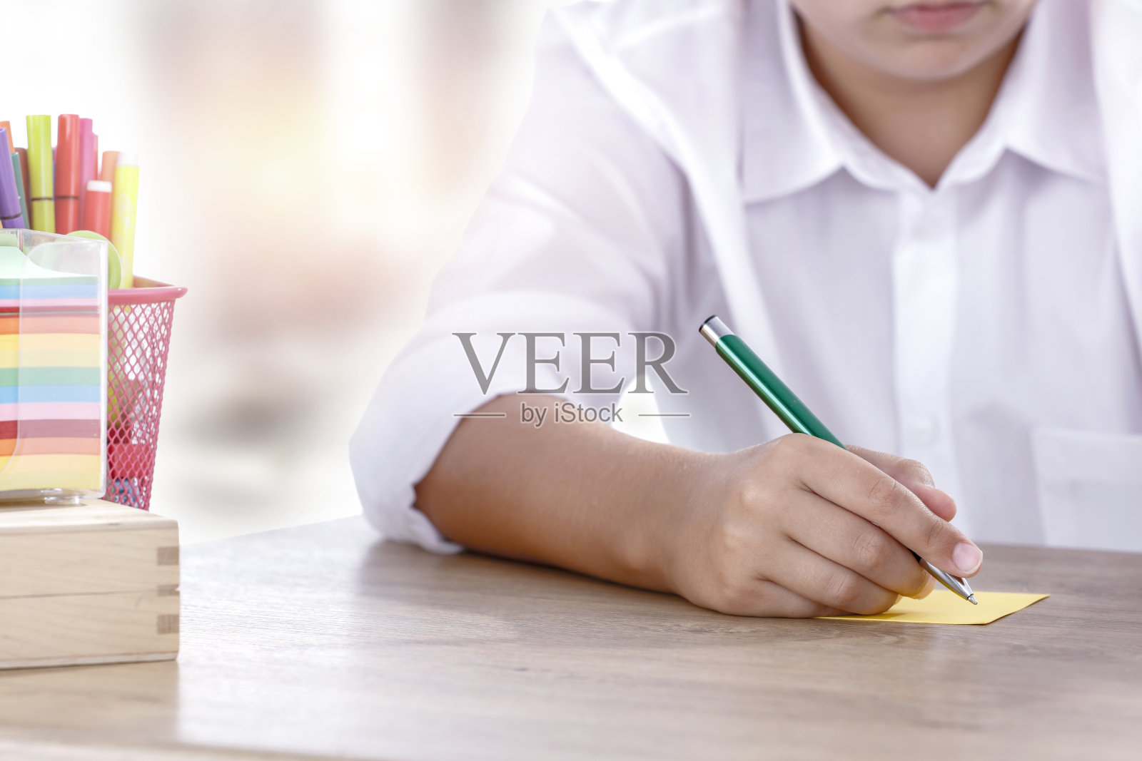 小学生坐在课桌前写纸条。木制桌子和文具及复印空间。照片摄影图片