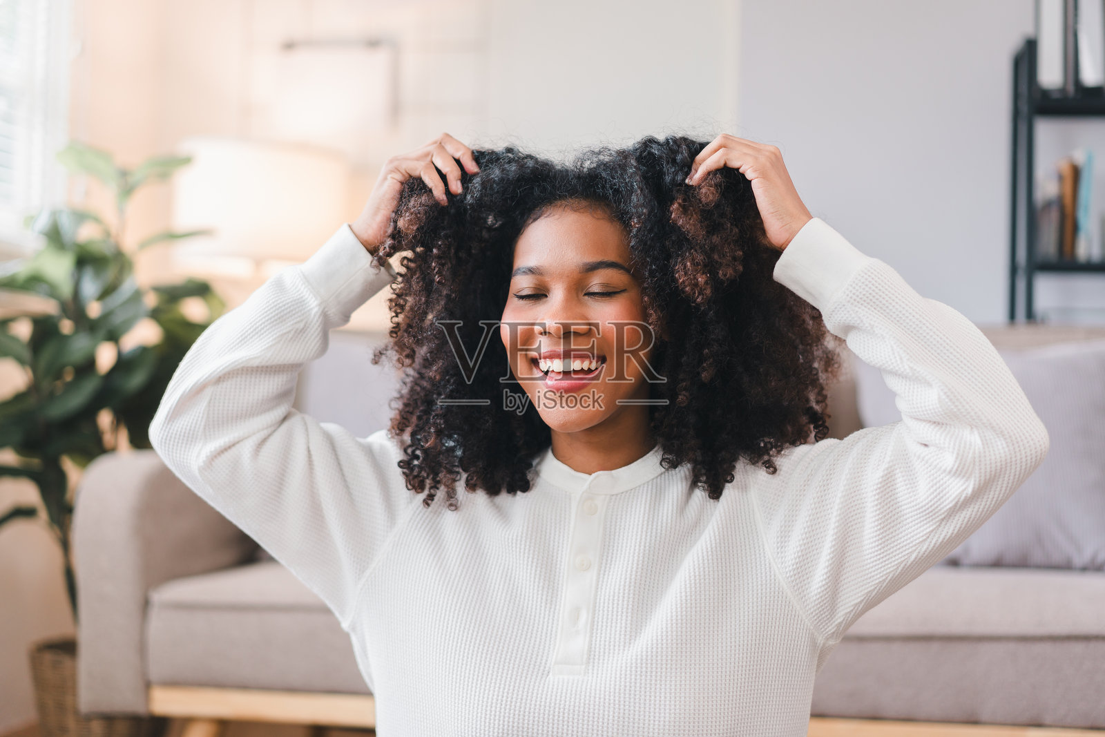 兴奋的非裔美国妇女在家里摆弄卷发。照片摄影图片