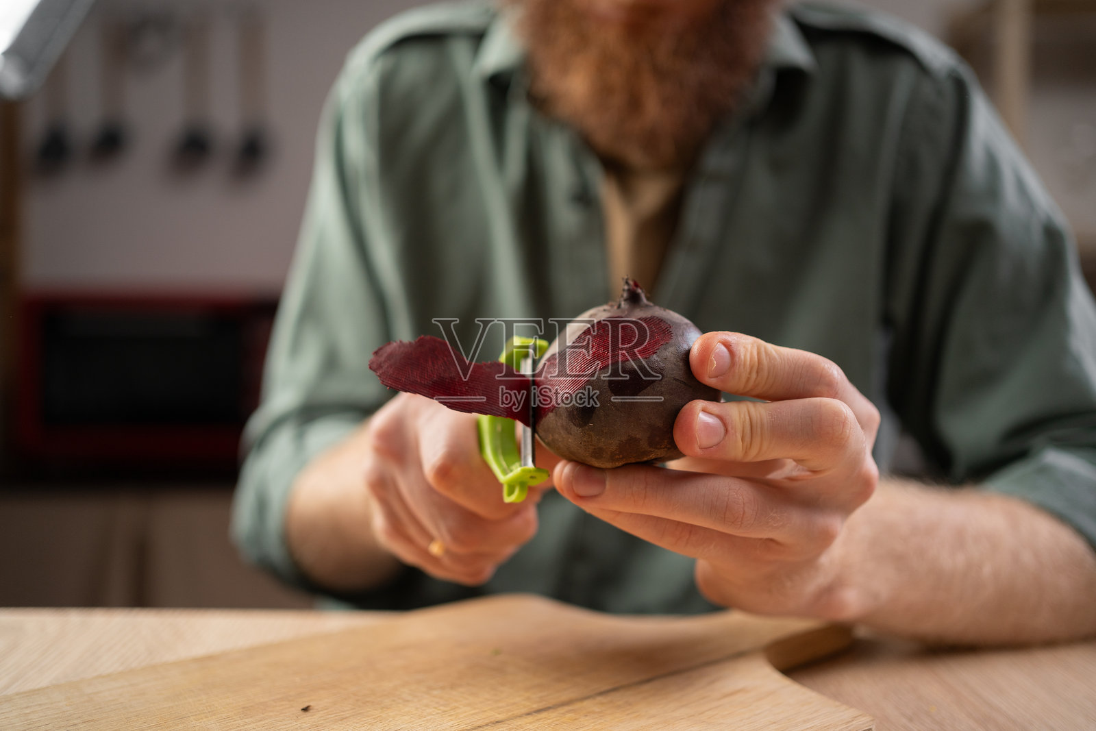 一名男子在厨房用蔬菜削皮器削甜菜根。家庭烹饪照片摄影图片