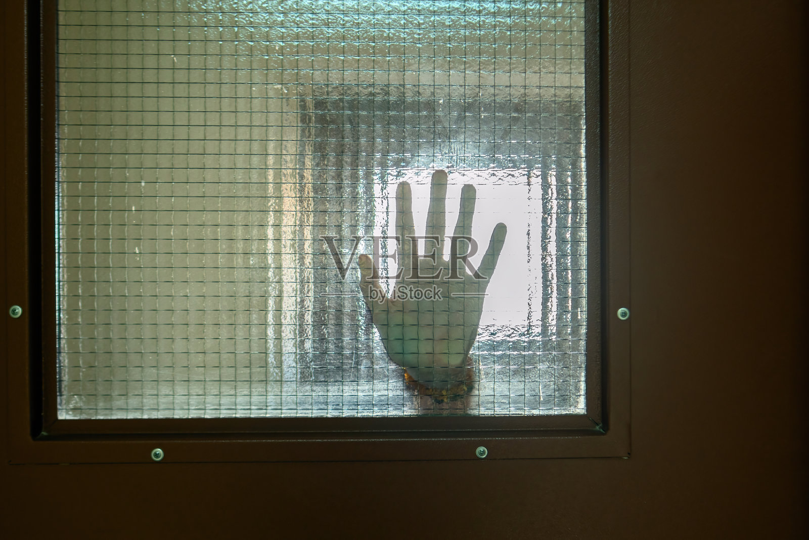 用手压在网格图案的玻璃上，象征着人与人之间的联系和结构障碍的交集，反映了脆弱、孤立和对亲密的渴望照片摄影图片