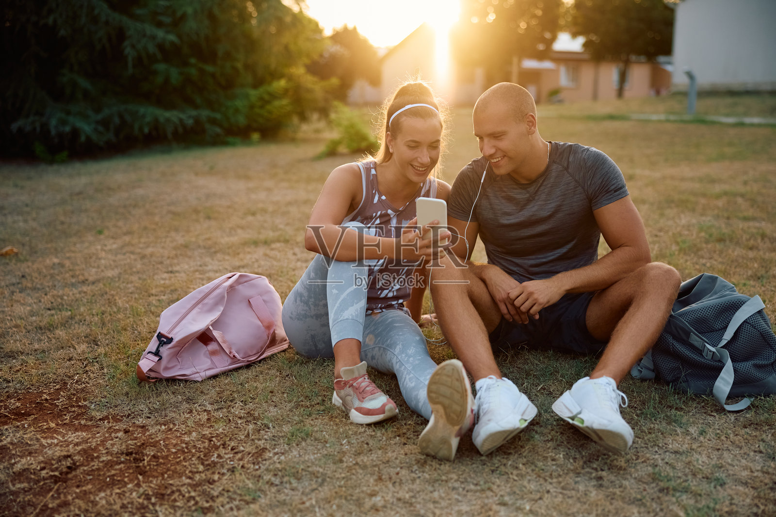 年轻的运动夫妇在日落时分用智能手机听着耳机上的音乐放松。照片摄影图片