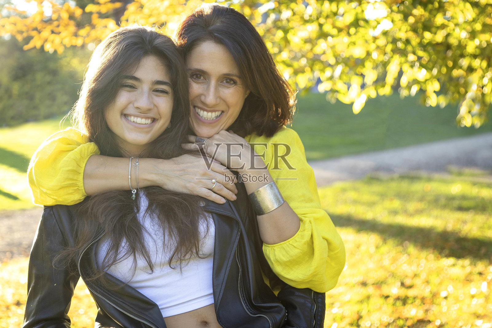 母亲和女儿在阳光明媚的公园里拥抱微笑。照片摄影图片
