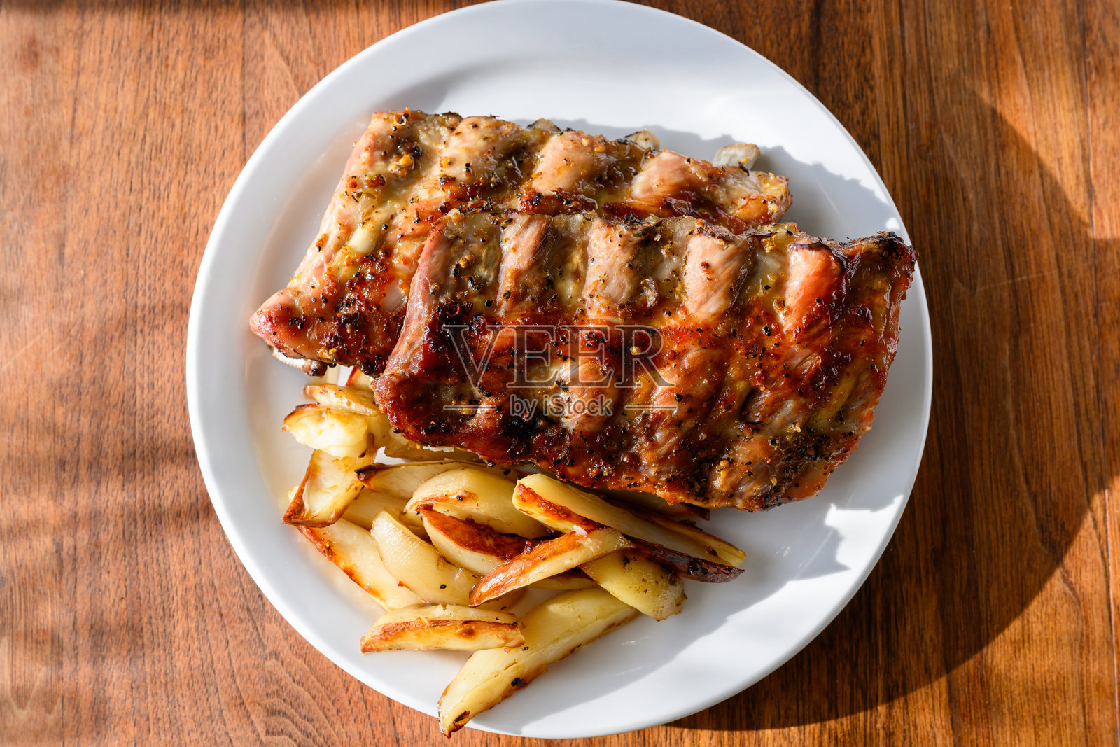 在傍晚温暖的阳光下，餐桌上的烤排骨和薯片照片摄影图片