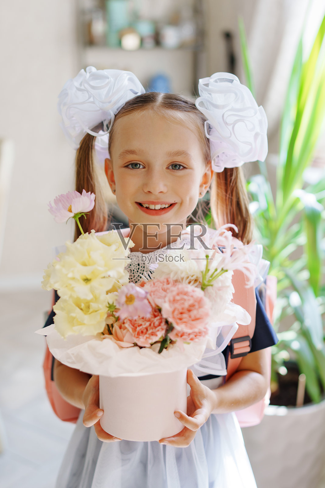 可爱的小女孩穿着校服，盒子里放着一束花。照片摄影图片