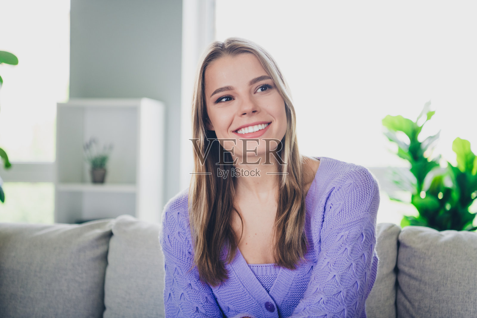 可爱开朗的女孩照片坐在沙发迷人的看着空旷的空间穿着紫色的衣服度过消遣宽敞的房子在室内房间照片摄影图片