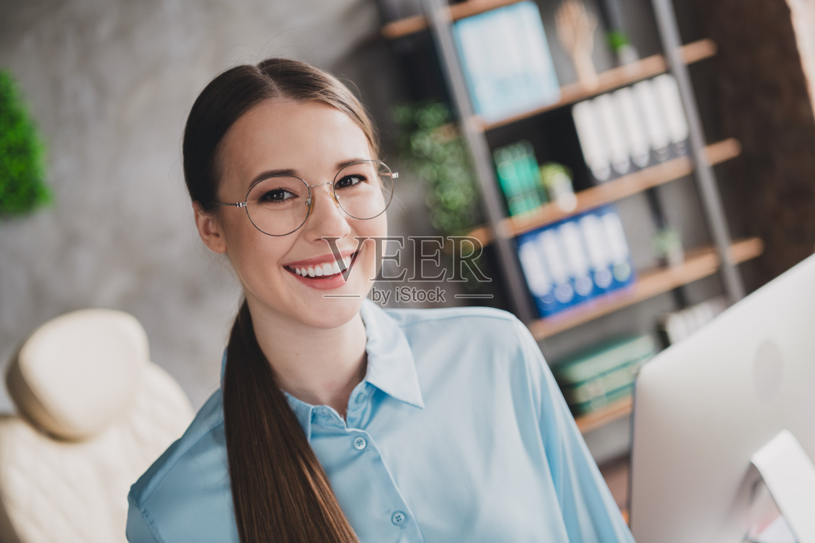 甜美迷人的女士助理的照片，穿着衬衫，戴着眼镜，微笑着在室内工作场所工作站照片摄影图片