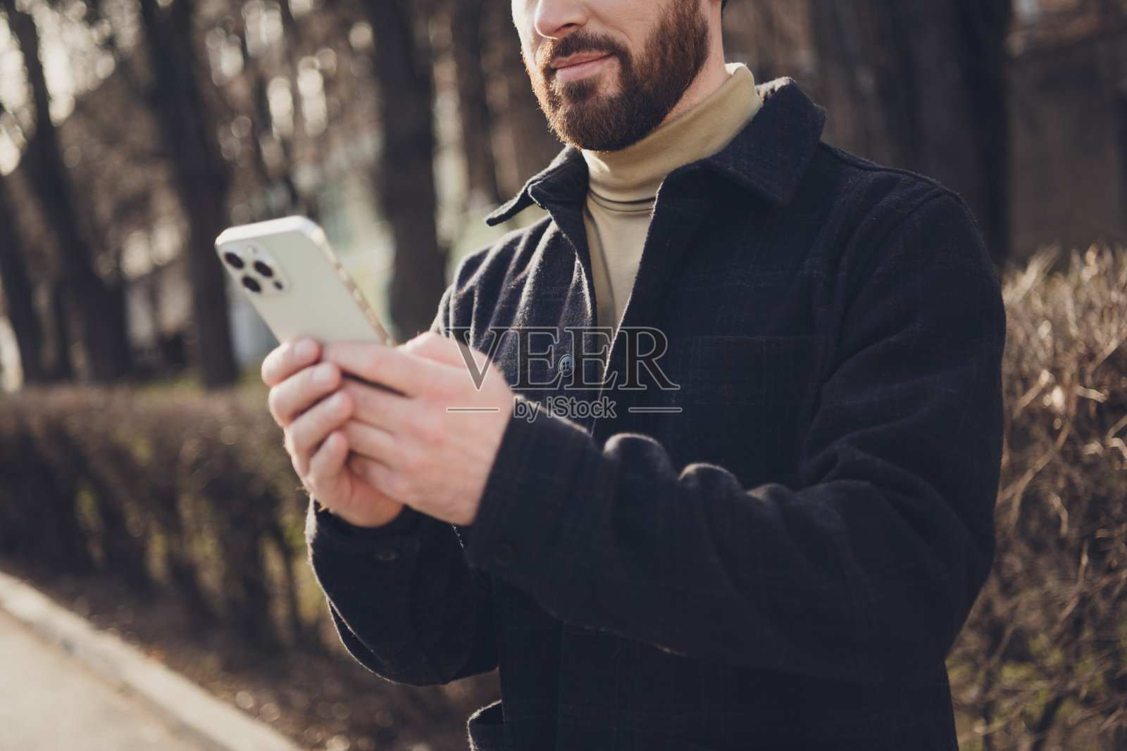 照片中英俊的成熟男子穿着时髦的衣服，使用设备走在户外的城市街道，秋天的一天照片摄影图片