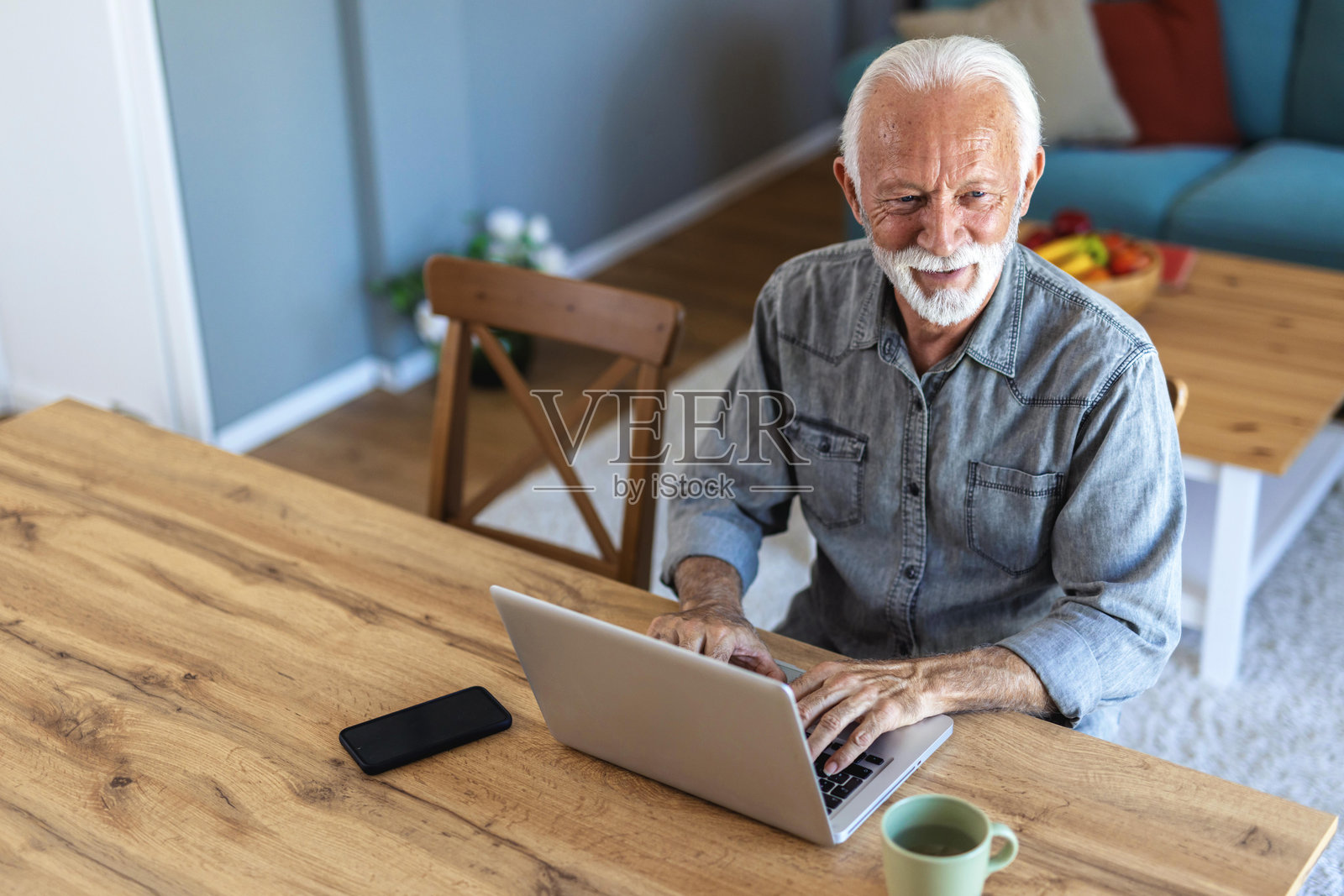 老人在公寓的办公桌上用笔记本电脑上网。一位老人坐在家里使用笔记本电脑的剪辑镜头。照片摄影图片