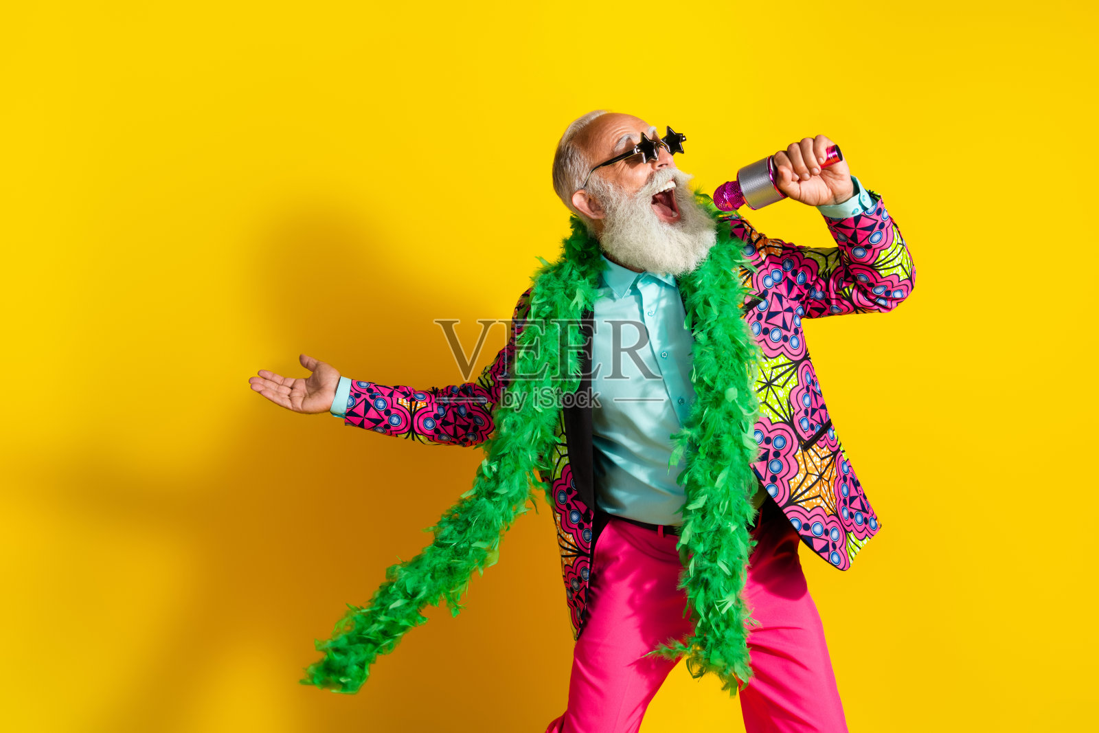 照片中古怪的老年歌手明星形状的太阳镜唱歌穿鲜艳的衣服孤立在黄色的背景照片摄影图片