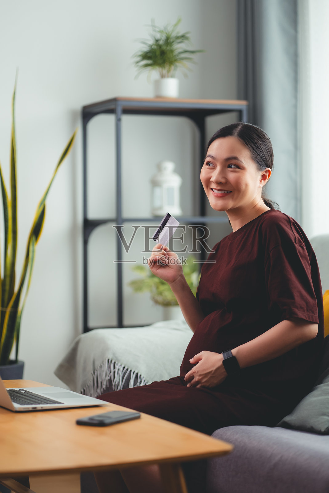 亚洲孕妇喜欢坐在家里的客厅里用笔记本电脑和信用卡进行网上购物。照片摄影图片