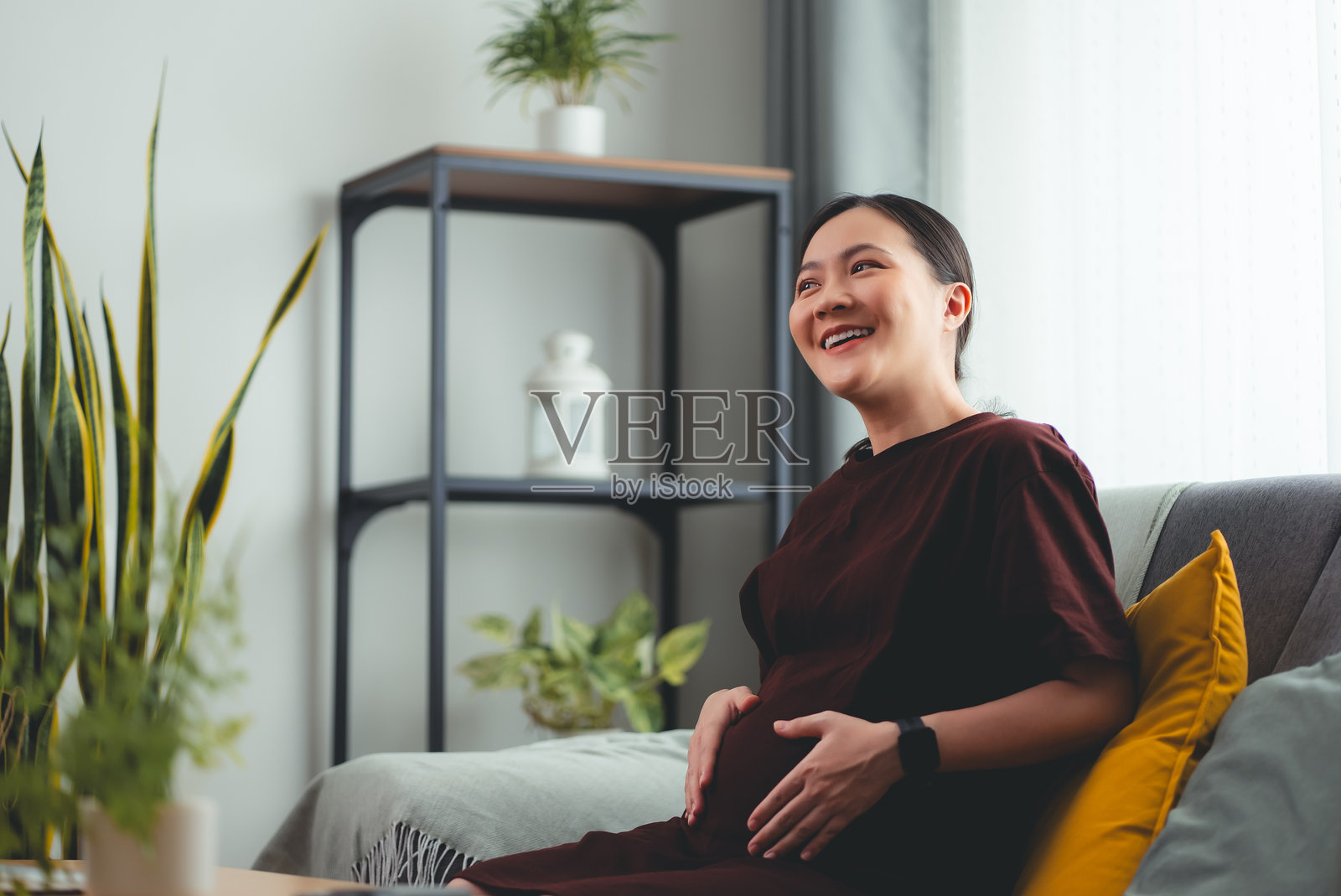 亚洲孕妇喜欢坐在家里客厅的沙发上放松。照片摄影图片
