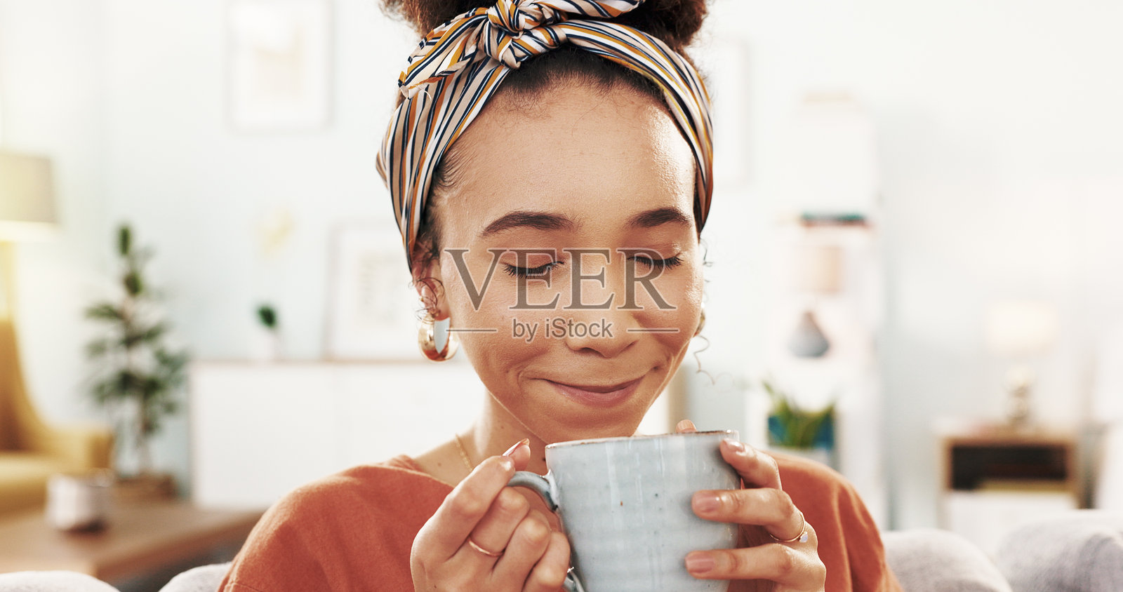 快乐的女人，在沙发上喝咖啡，放松一下，在家里喝饮料或早晨。年轻，面带微笑的女性，家里沙发上有咖啡、卡布奇诺或拿铁的味道照片摄影图片