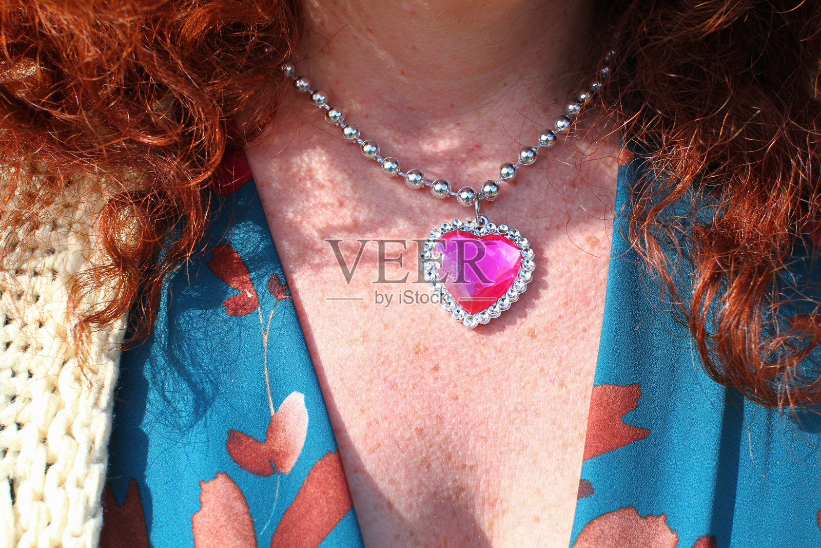 红头发女人的颈部细节与粉红色的心吊坠项链和绿松石连衣裙照片摄影图片