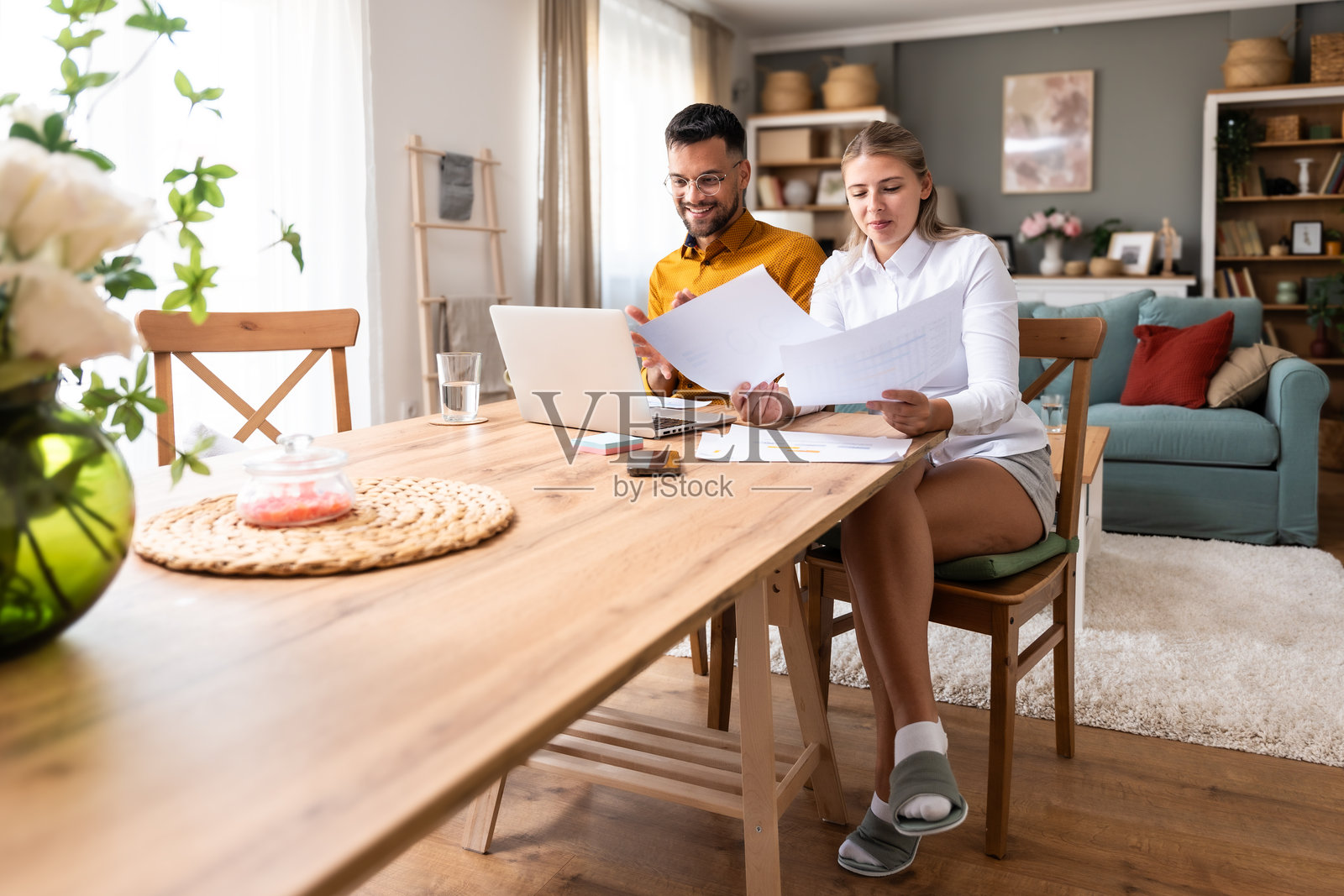 在家工作。年轻的自由职业者夫妇在家里办公室用笔记本电脑与客户进行视频通话，用打印在纸上的销售图表显示业务改善的统计数据。照片摄影图片