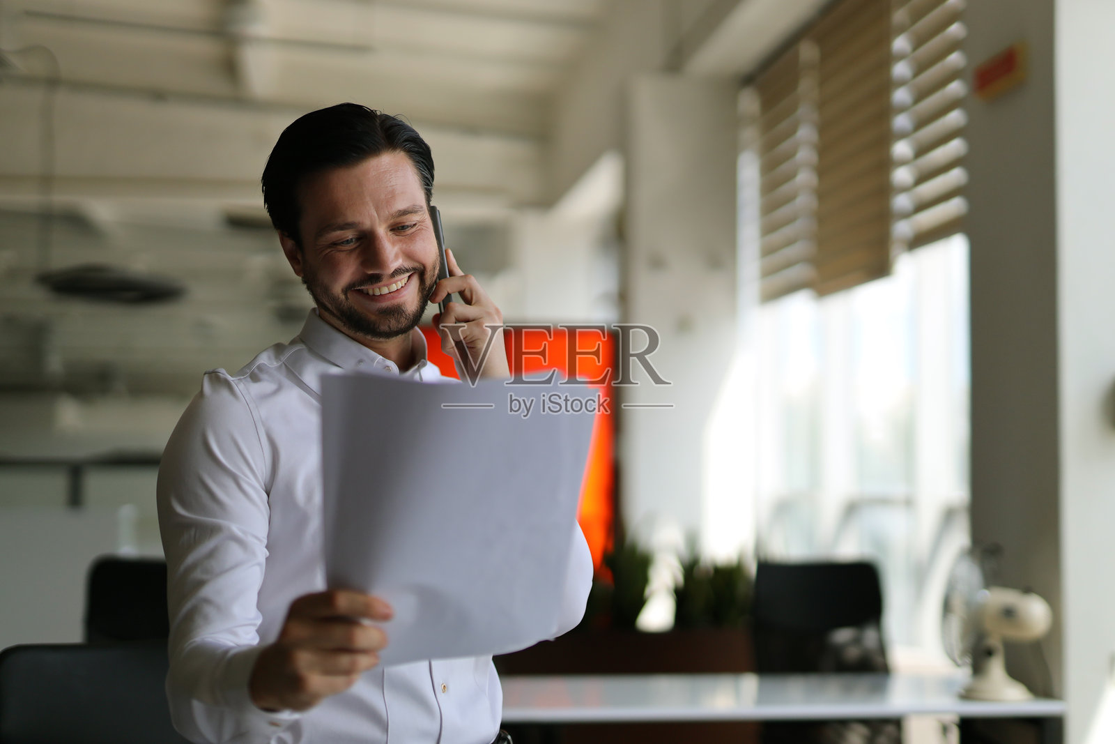 一个男人拿着一张纸在打电话。他面带微笑，心情很好照片摄影图片