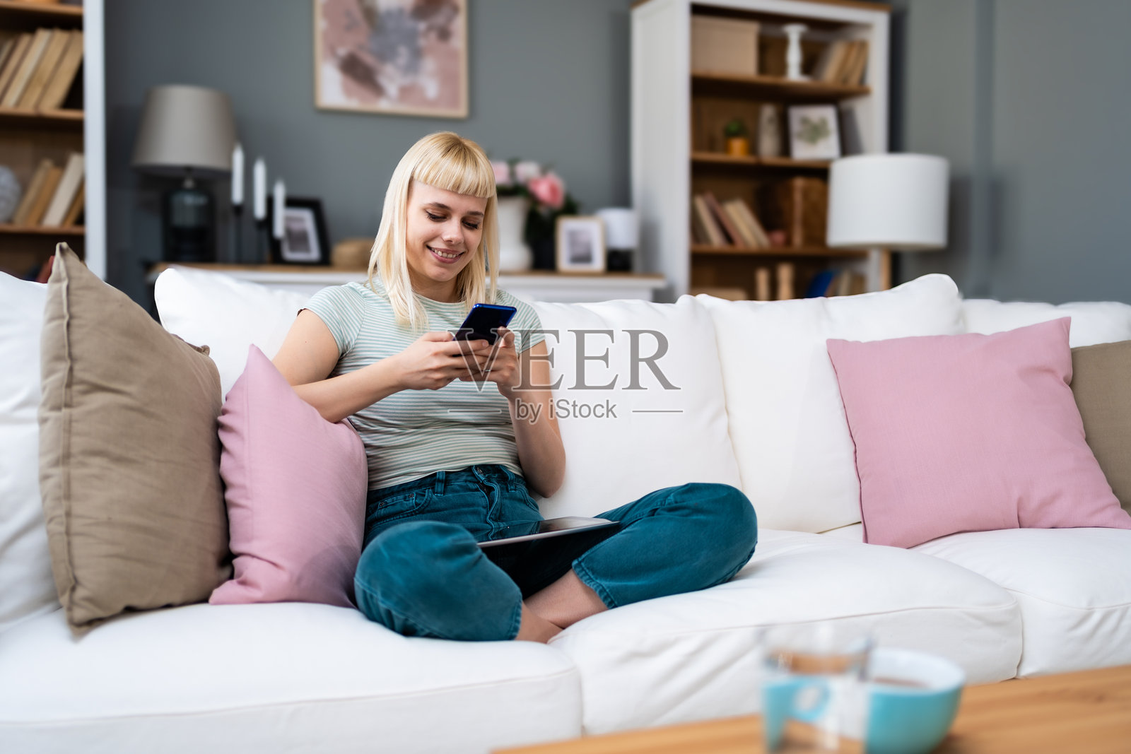 快乐放松的年轻女子坐在沙发上使用手机，微笑的女士笑着拿着智能手机，看着手机，享受在移动应用程序中进行在线电子商务购物或在线约会。照片摄影图片