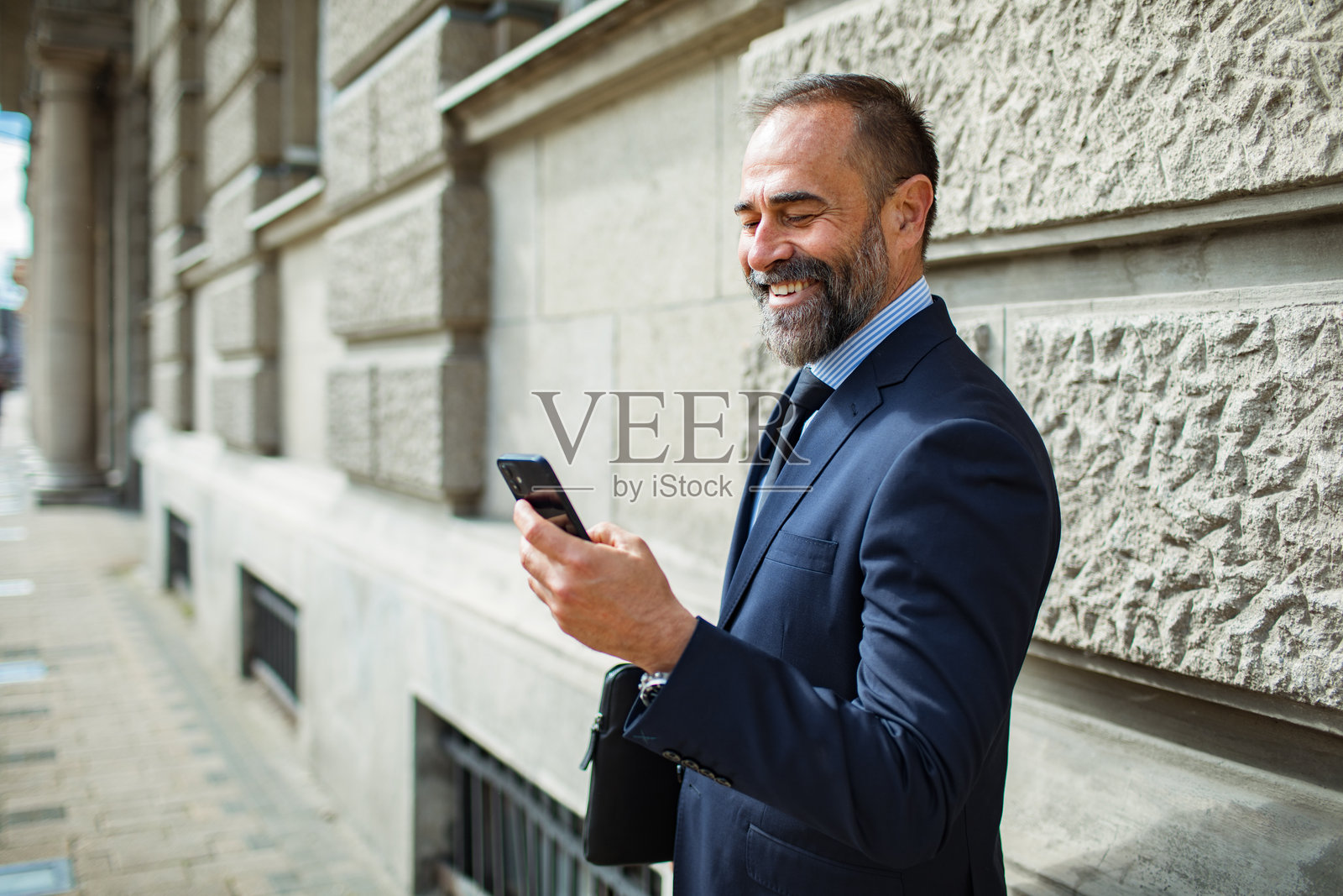 中年商人微笑着在城市里使用智能手机照片摄影图片
