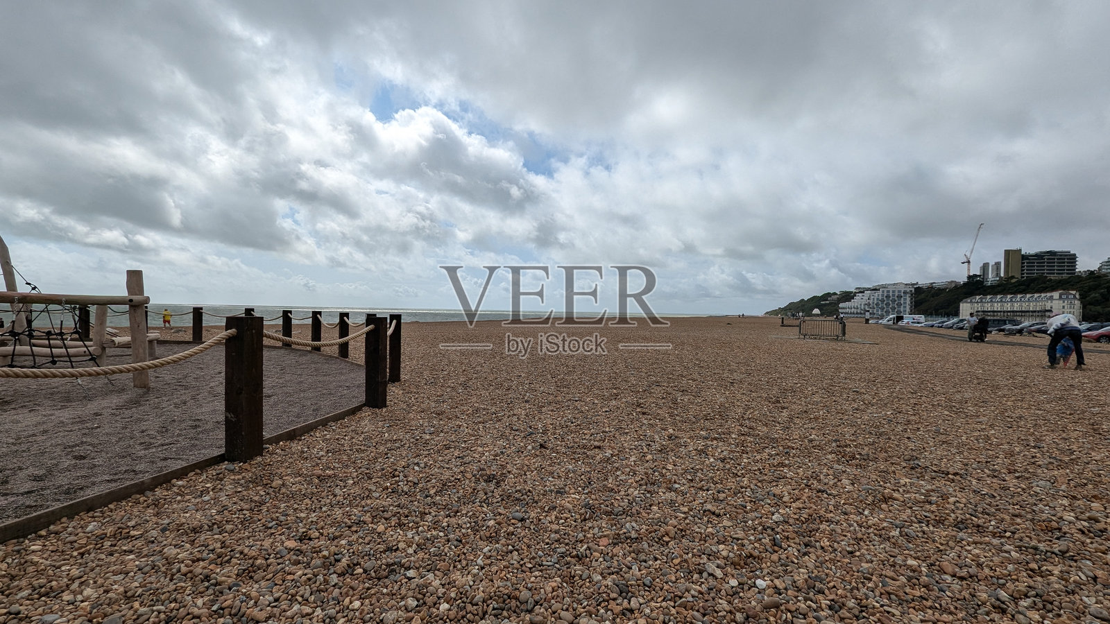 灰色天空的石质海滩，儿童游乐场和远处的建筑物用绳子隔开照片摄影图片