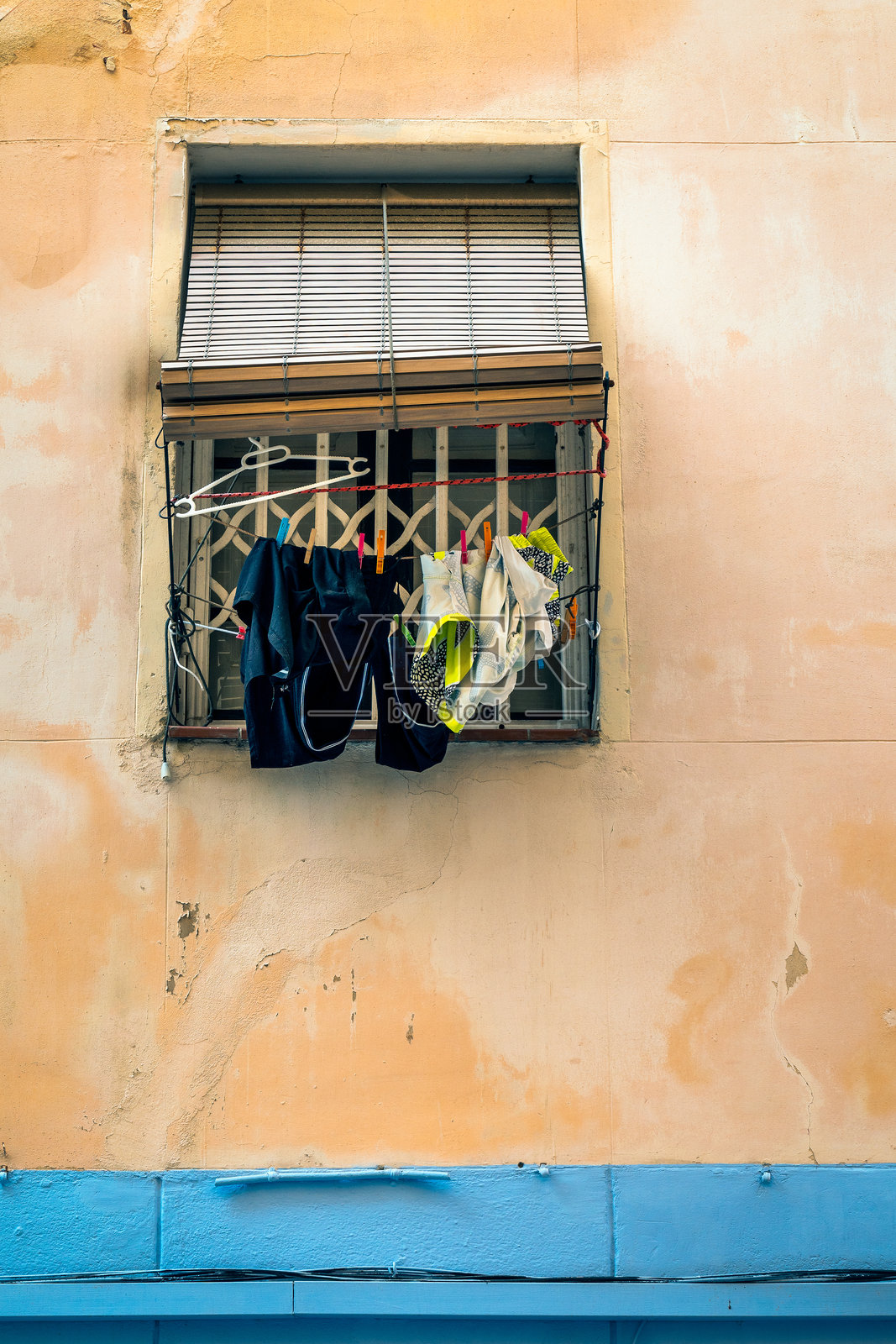 通过在充满活力的墙上的窗框后面晒衣服的简单动作，一瞥日常的城市生活。西班牙巴塞罗那照片摄影图片