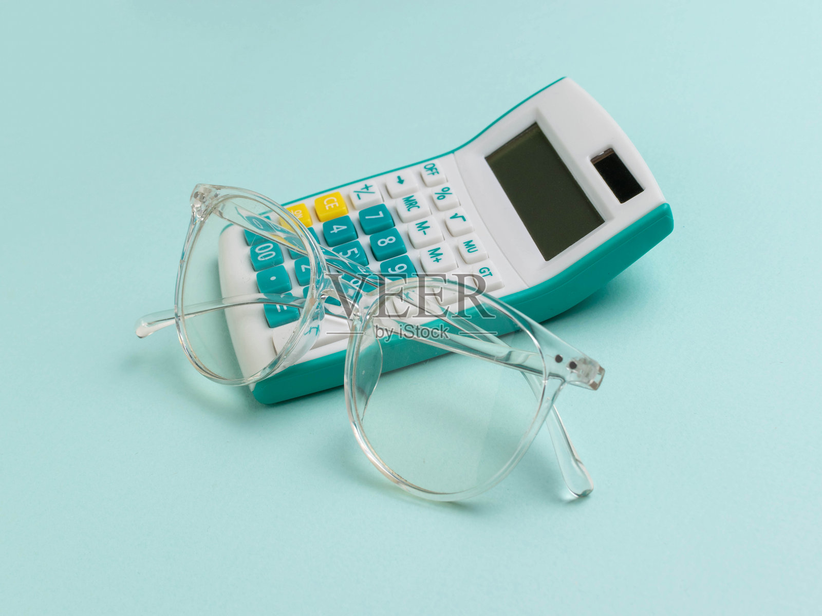 透明眼镜休息在蓝绿色计算器对浅蓝色背景照片摄影图片