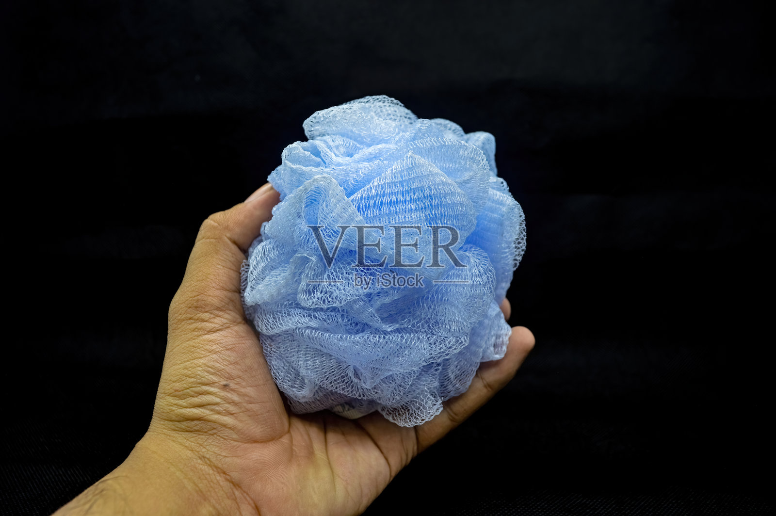 一只手拿着蓝色的沐浴海绵。照片摄影图片