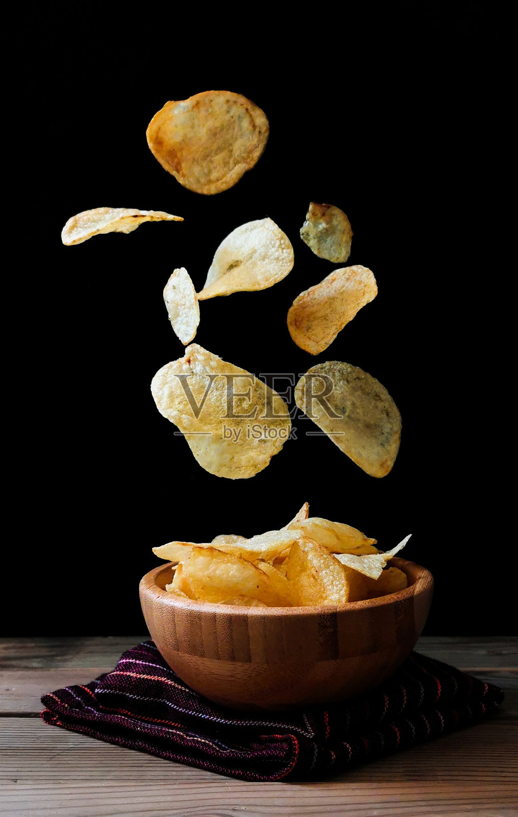 薯片落在碗里的特写，黑色背景照片摄影图片