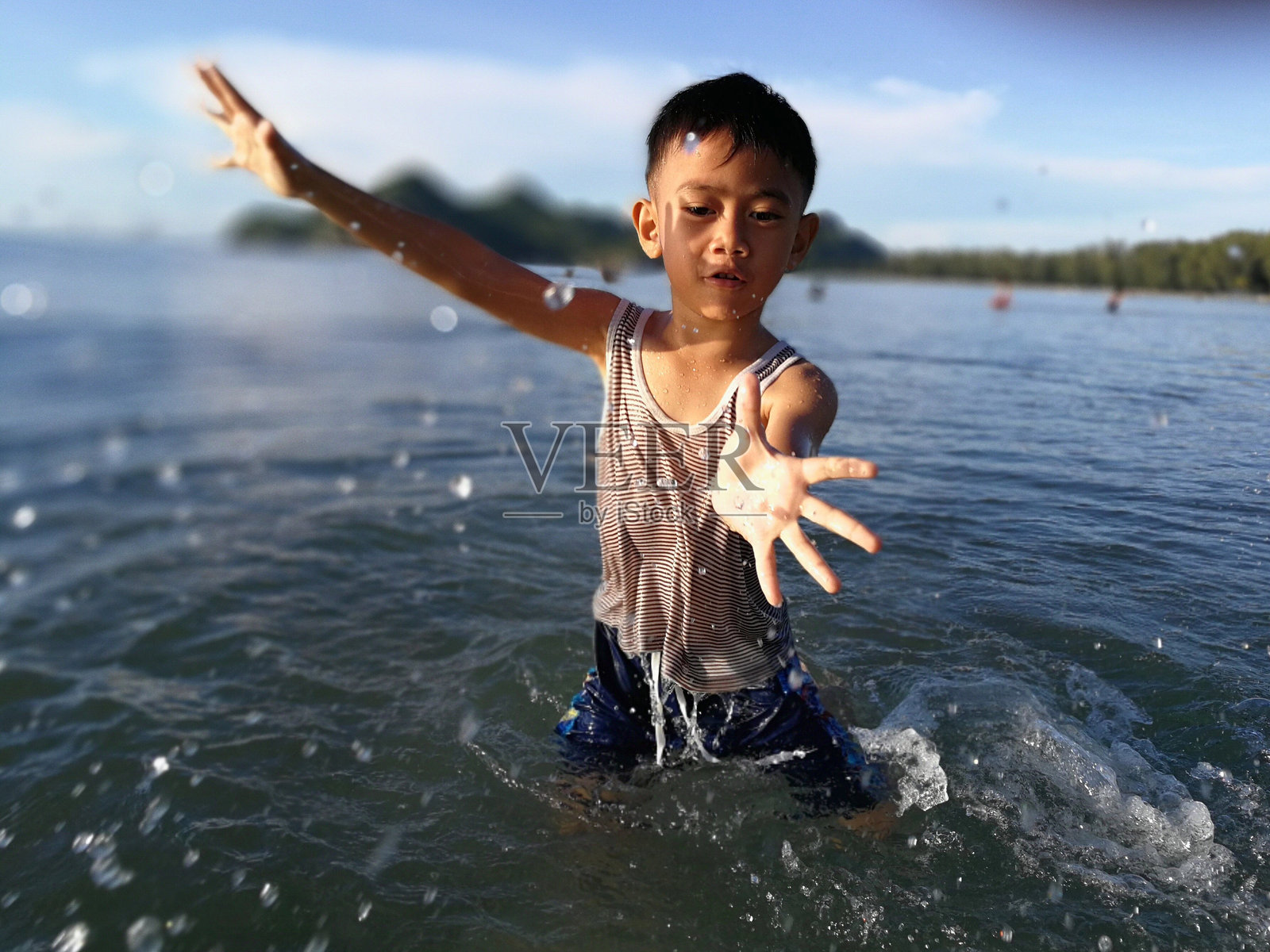 阳光明媚的日子里，男孩在海中站立，背景是天空。照片摄影图片