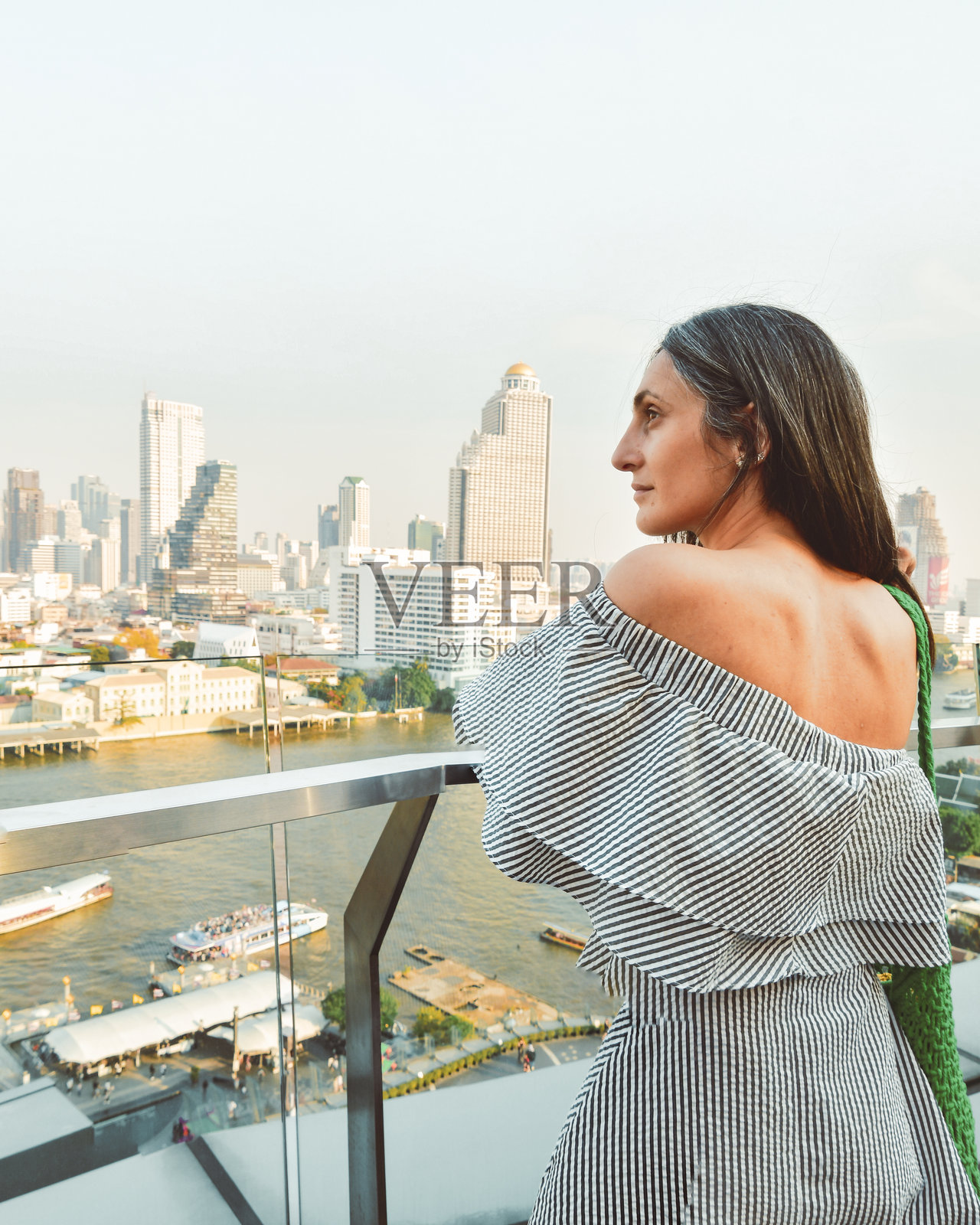 泰国曼谷 - 2024年2月11日：在东南亚热门旅游目的地曼谷，阳光明媚的炎热天气中，女游客在购物中心著名的河景观景点前拍照。照片摄影图片