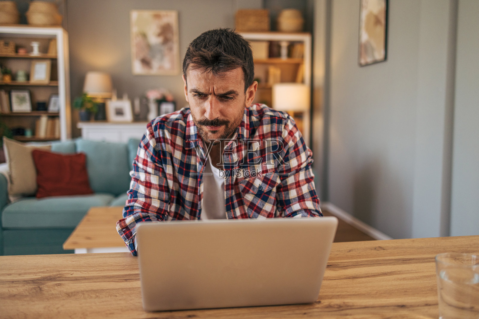 一个中年男子坐在家里客厅的桌子旁，用着笔记本电脑。照片摄影图片