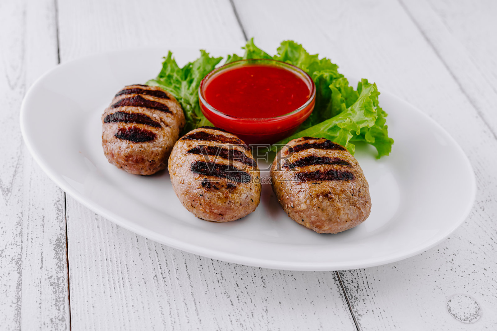 白色的桌子上，白色的盘子里放着三个蘸着红酱的烤肉丸照片摄影图片