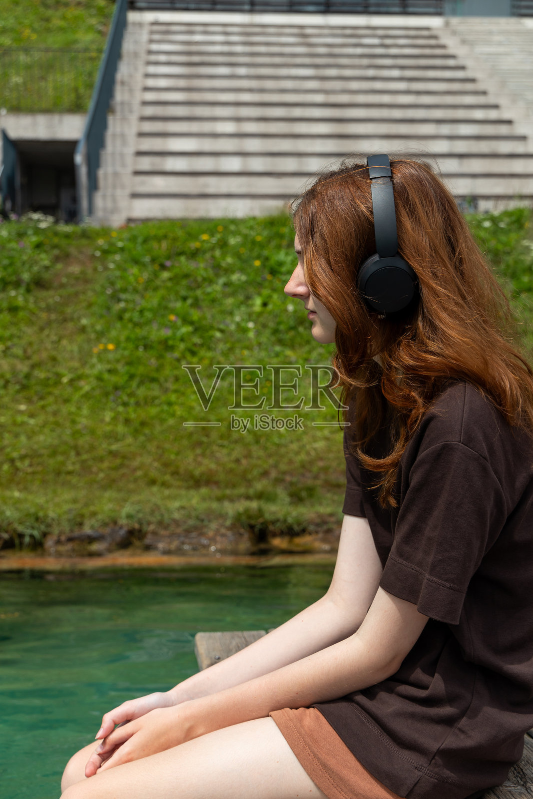 戴着耳机的女孩坐在码头上听着湖边的音乐。照片摄影图片