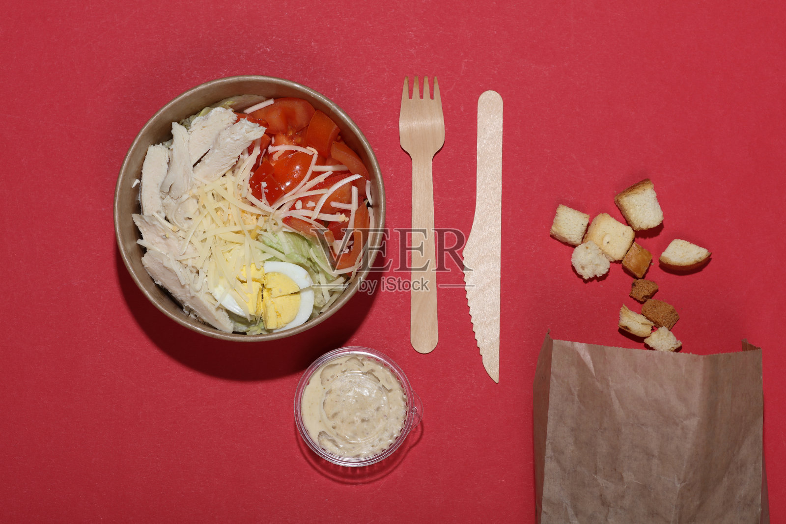 凯撒沙拉装在一次性硬纸板容器里，红色背景是食品配件照片摄影图片