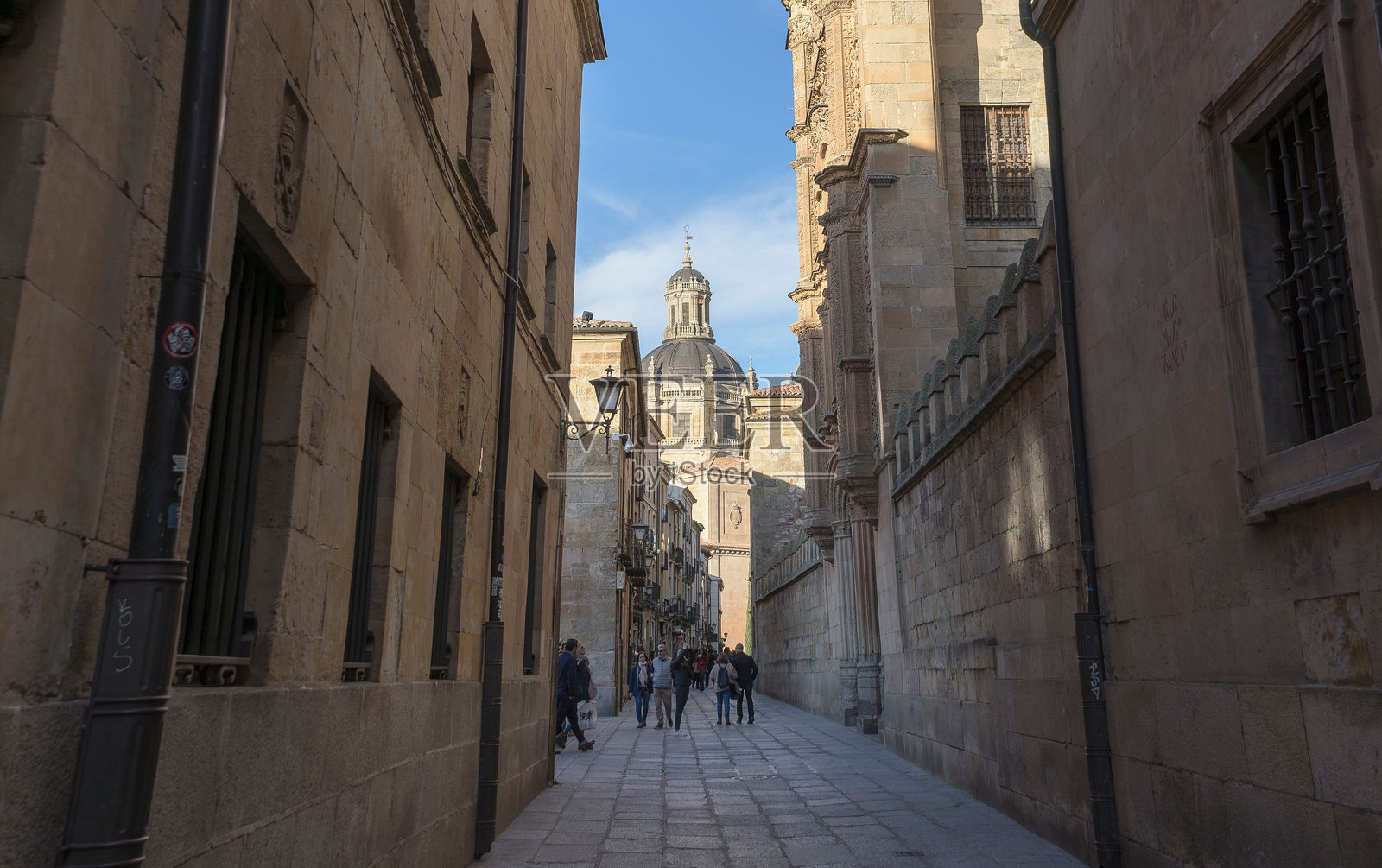 西班牙萨拉曼卡的一条狭窄鹅卵石街道上，人们正在行走。照片摄影图片