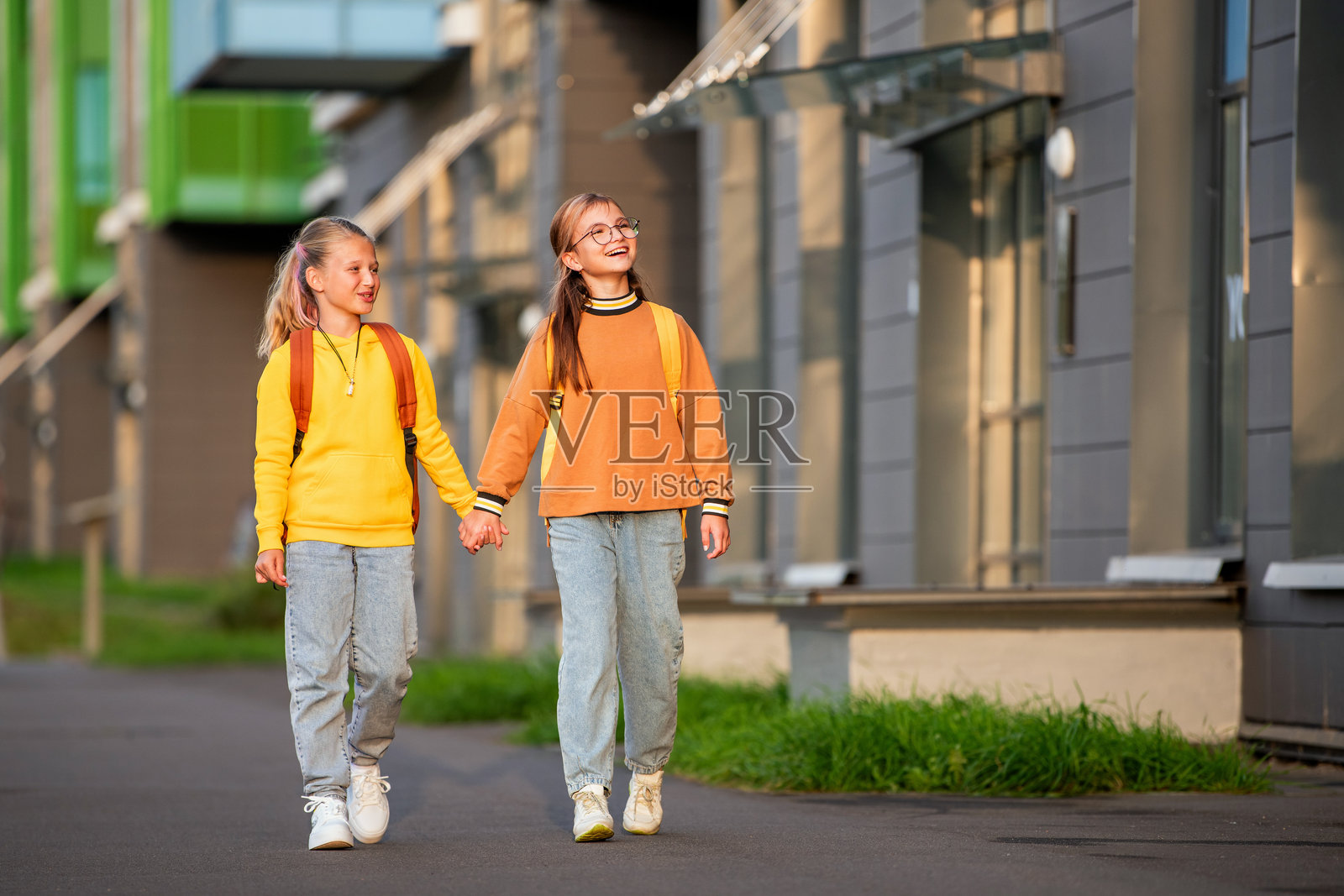 两个快乐的孩子背着书包沿着阳光明媚的城市街道走去。照片摄影图片