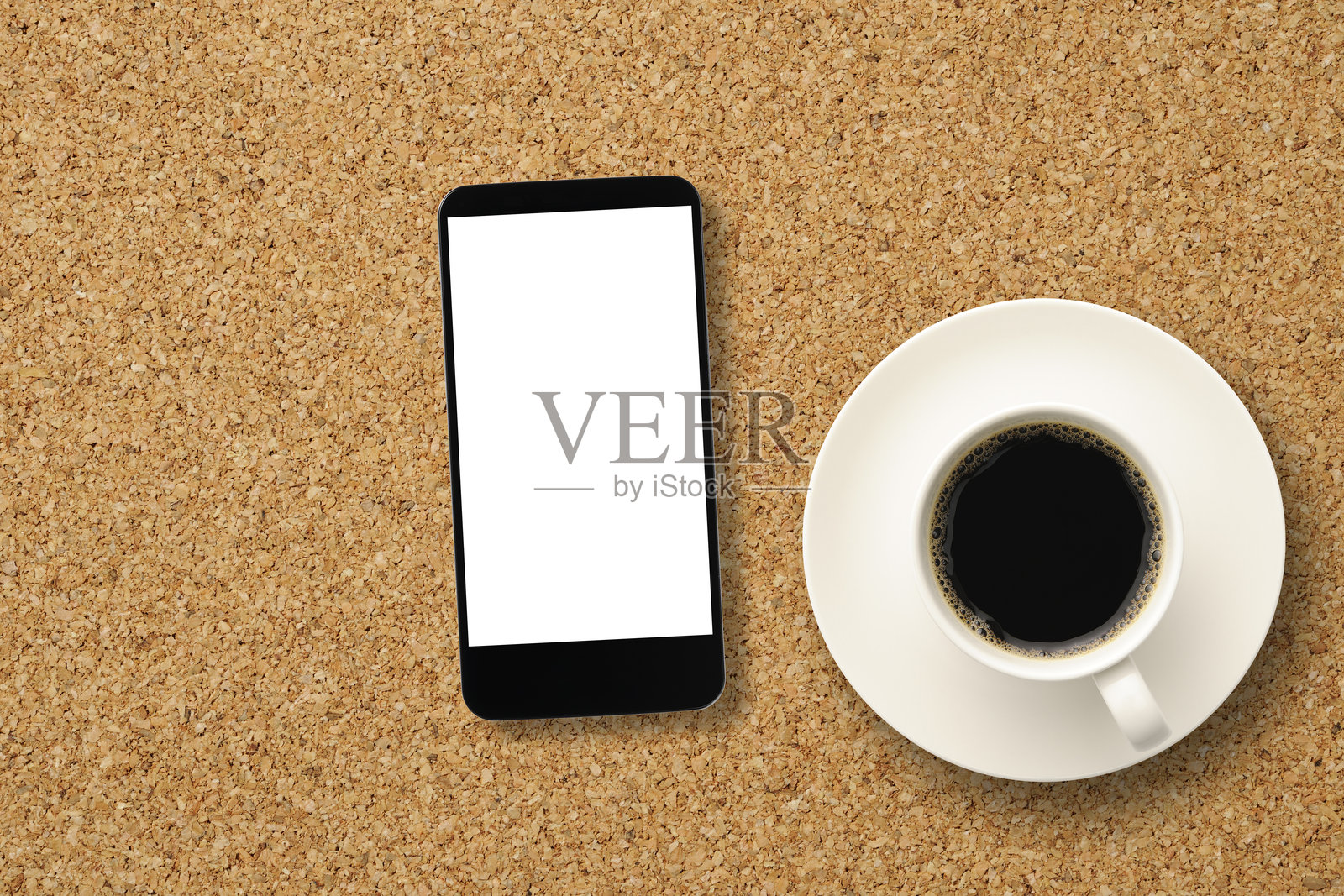 一杯咖啡放在软木桌上，旁边有一部空白的智能手机照片摄影图片
