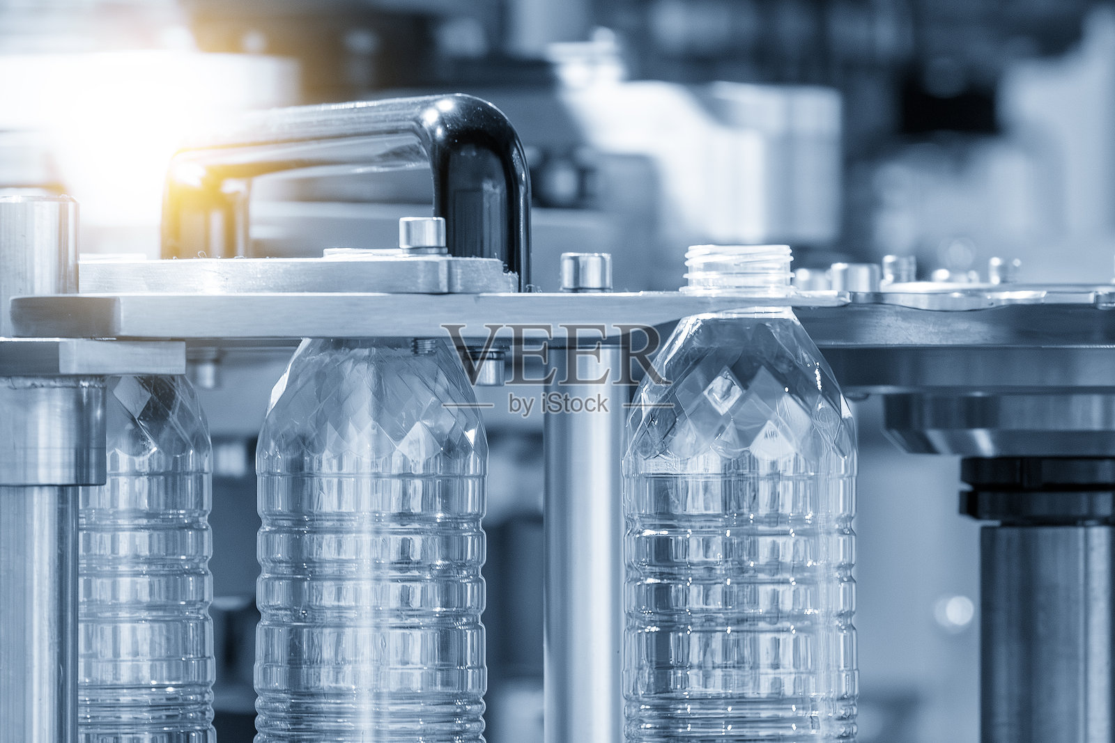 在淡蓝色场景中，使用吹塑机制造饮用水瓶的过程，伴有灯光效果。照片摄影图片