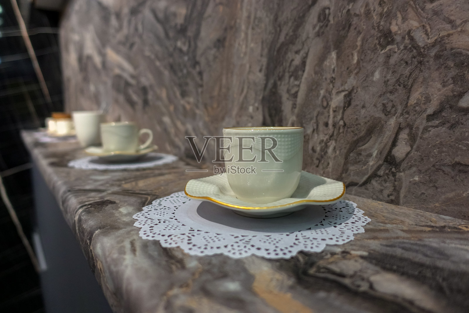 一个白色的杯子和碟子，以及一块蕾丝餐巾，放在大理石窗台上。照片摄影图片