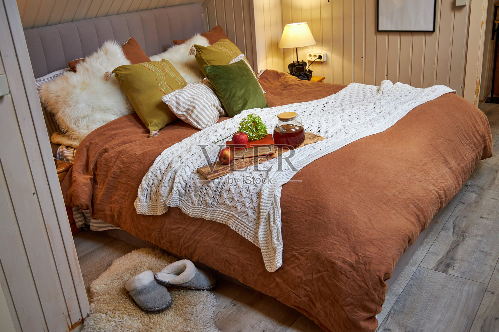 Interior of a modern bedroom, a double bed with a beige linen coverlet and colorful pillows and white plaid on which stands a tray with tea and fruit照片摄影图片