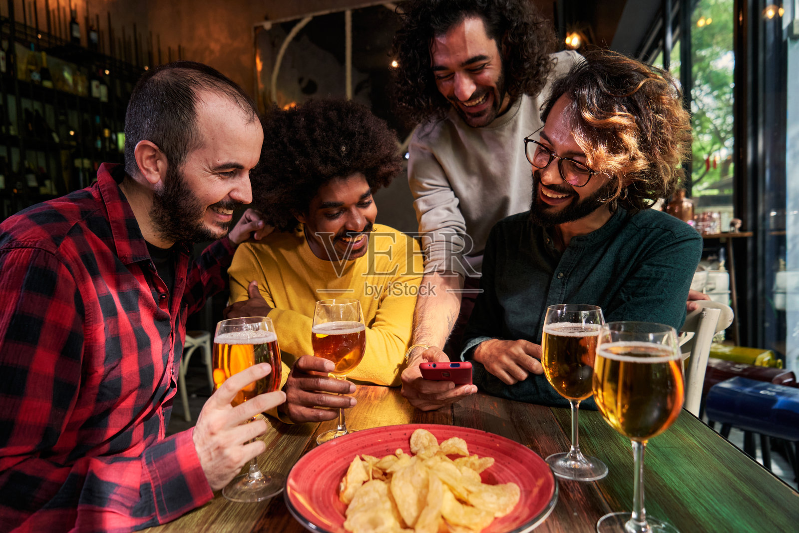 一群男性朋友在酒吧里玩得开心，喝着啤酒，使用一部手机观看社交媒体。照片摄影图片