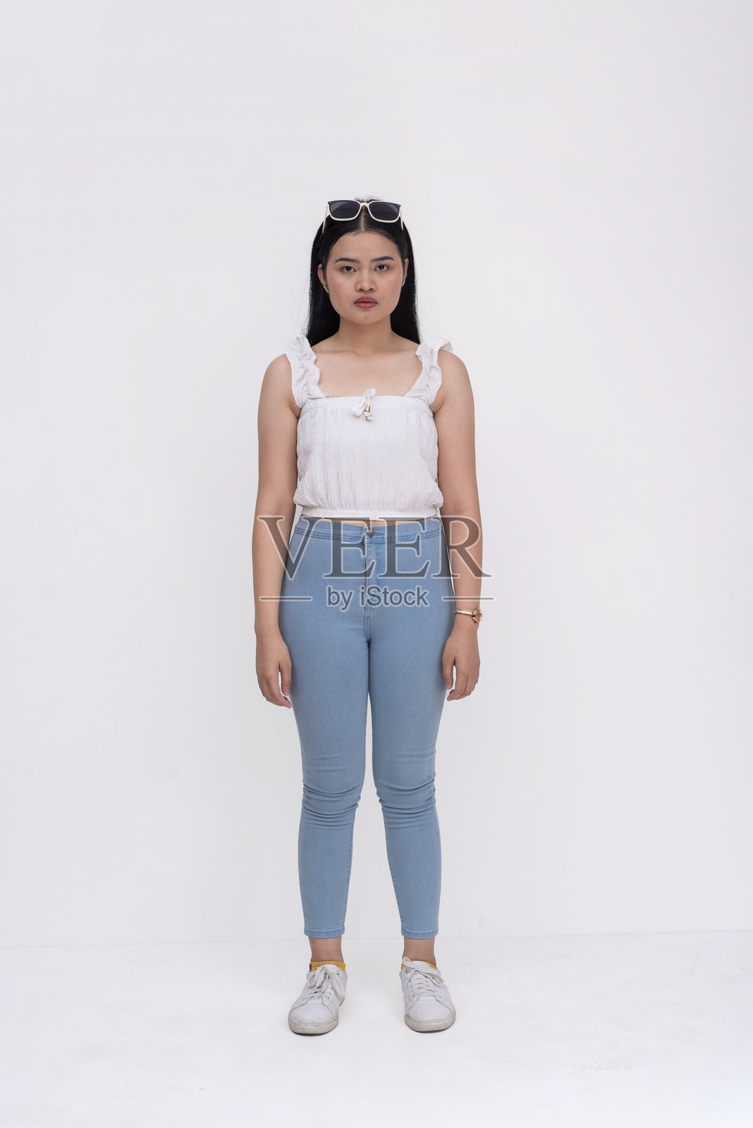 一位年轻的亚洲女性，留着中长发，穿着白色衬衫和浅蓝色牛仔裤。可能是一名大学生，表情严肃而冷静。背景为白色。照片摄影图片