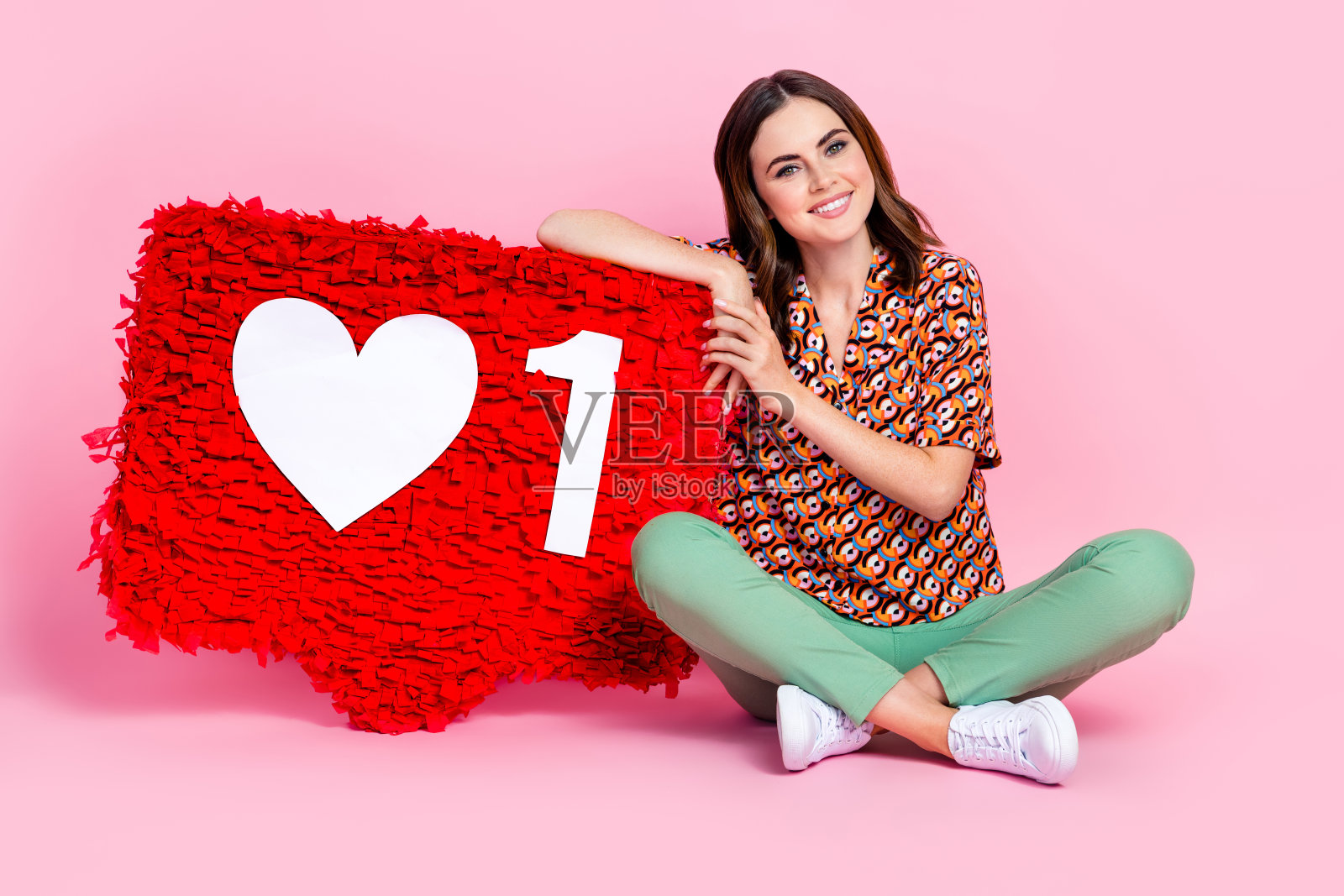 充满魅力和乐观的女孩坐在舒适的地方，旁边是一个大红色的皮纳塔通知图标，背景为粉色。照片摄影图片