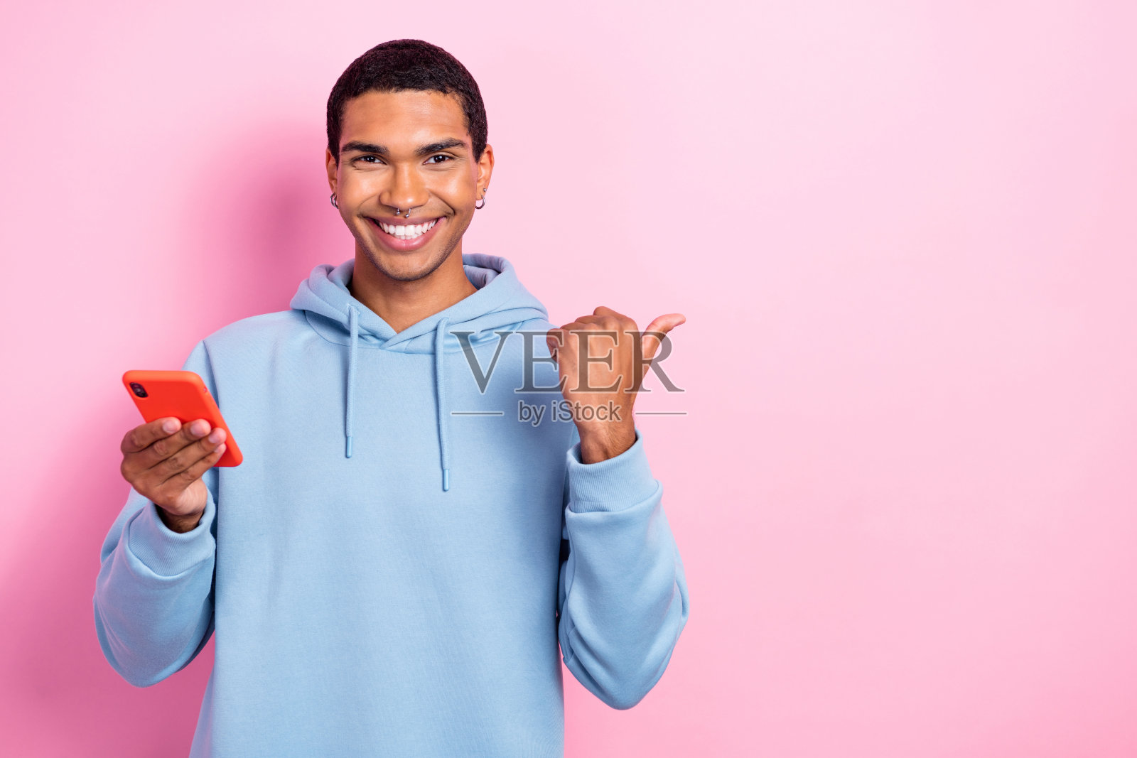 酷炫积极的男士手持电话，手指指向粉色背景上的空白处。照片摄影图片