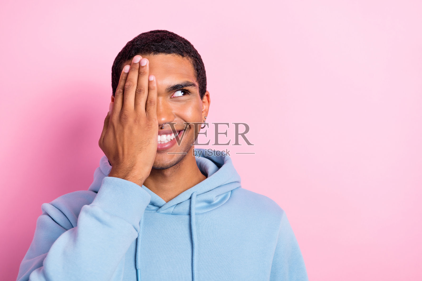 快乐满意的幽默男子用手掌遮住眼睛，检查视力，目光投向空旷的空间，背景为粉色，经过矫正的健康检查。照片摄影图片